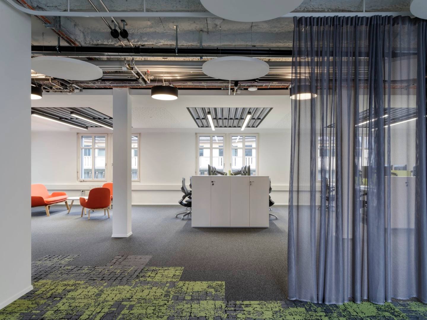 Pièce de coworking, moquette grise, mur blanc, rideau gris, fauteuil orange