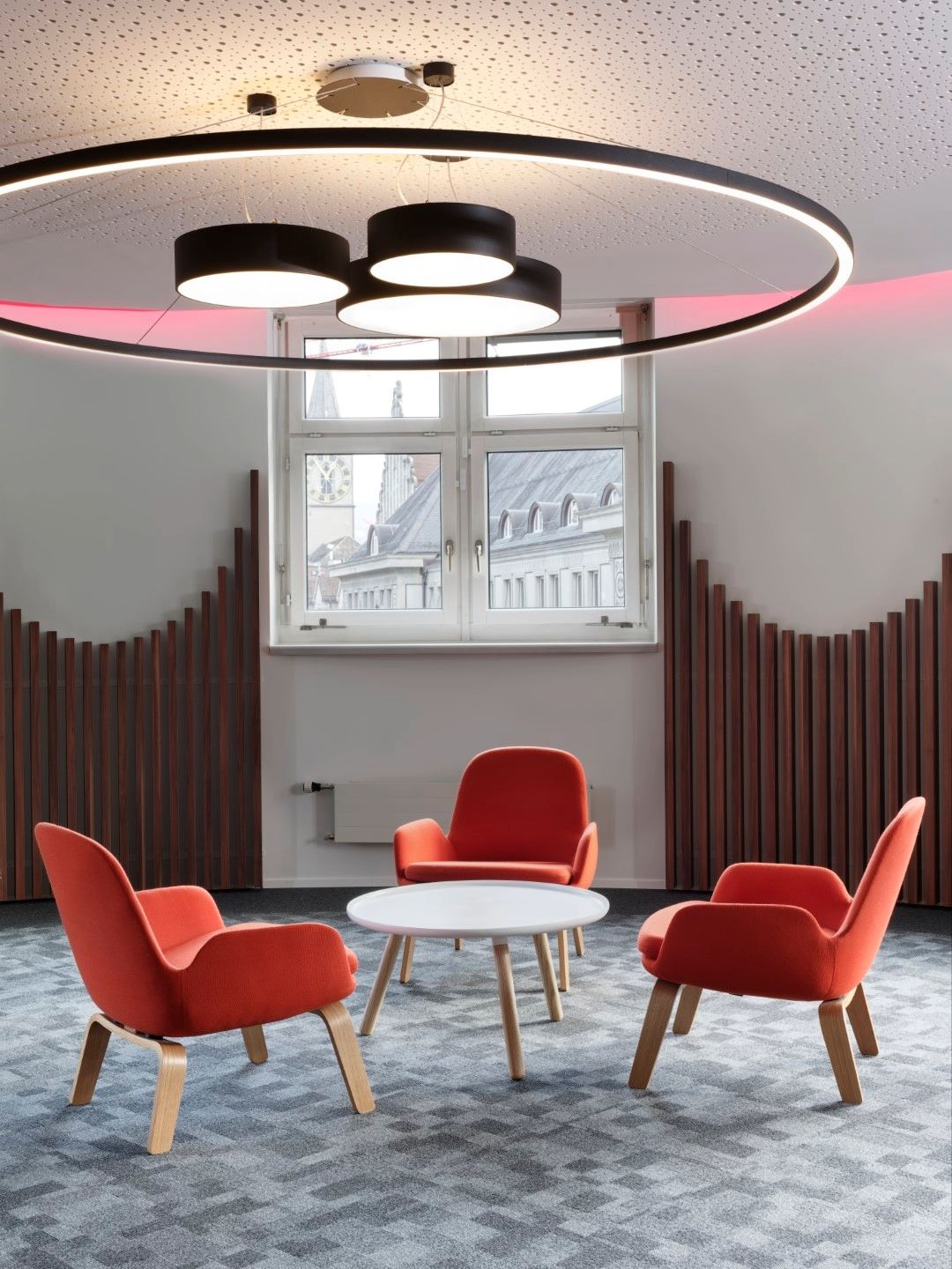 Pièce avec trois fauteuils orange et une table basse blanche, moquette grise, lustre noir