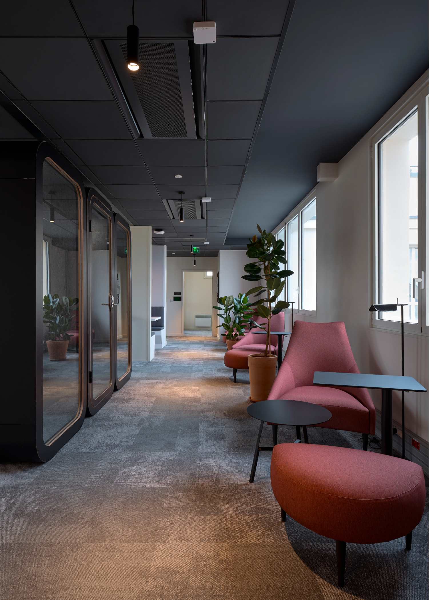 Espace de travail, moquette grise, plafond noir, fauteuil rouge et table basse noire métallique