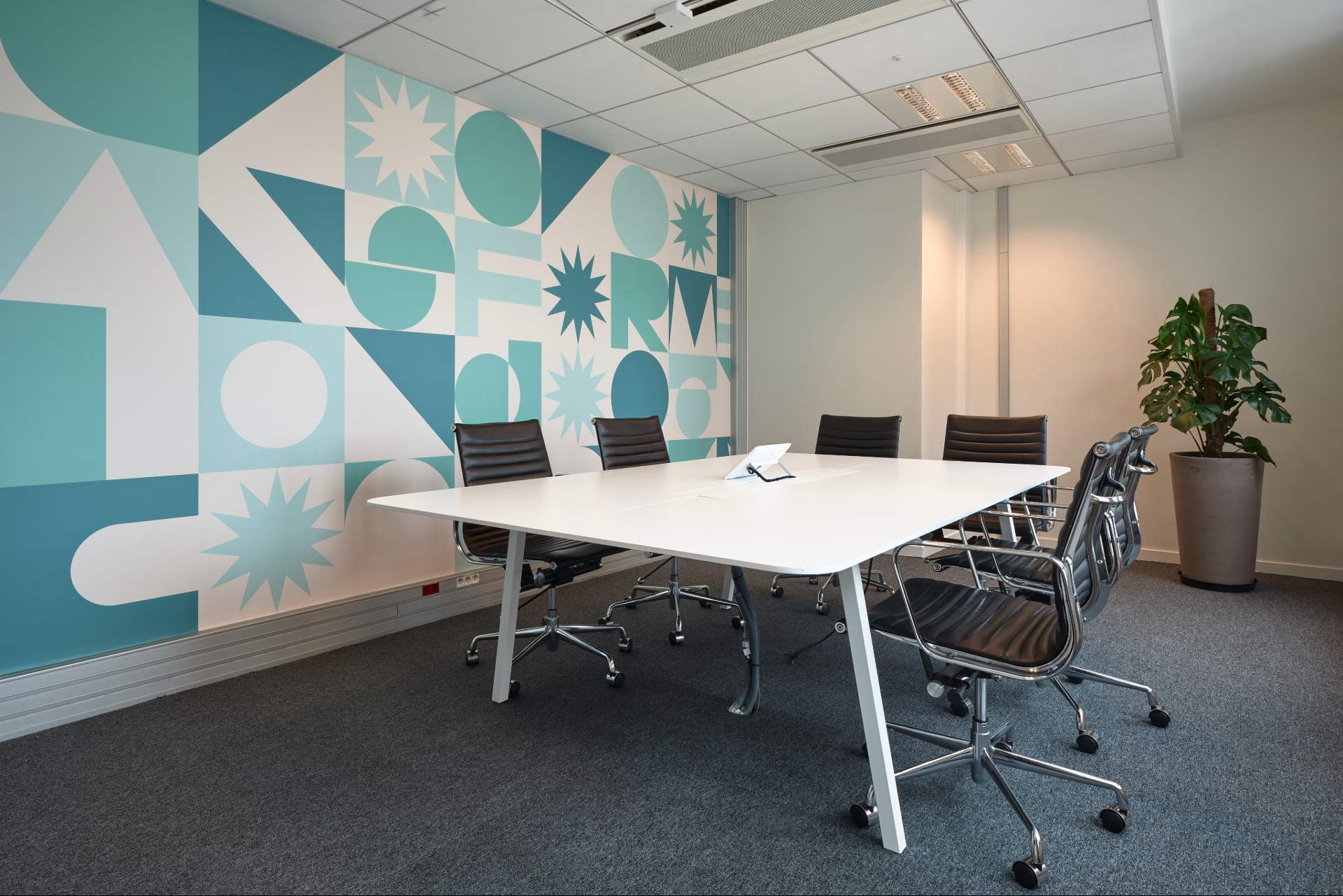 Salle de réunion, moquette grise, table blanche, chaises noires, décoration murale bleue