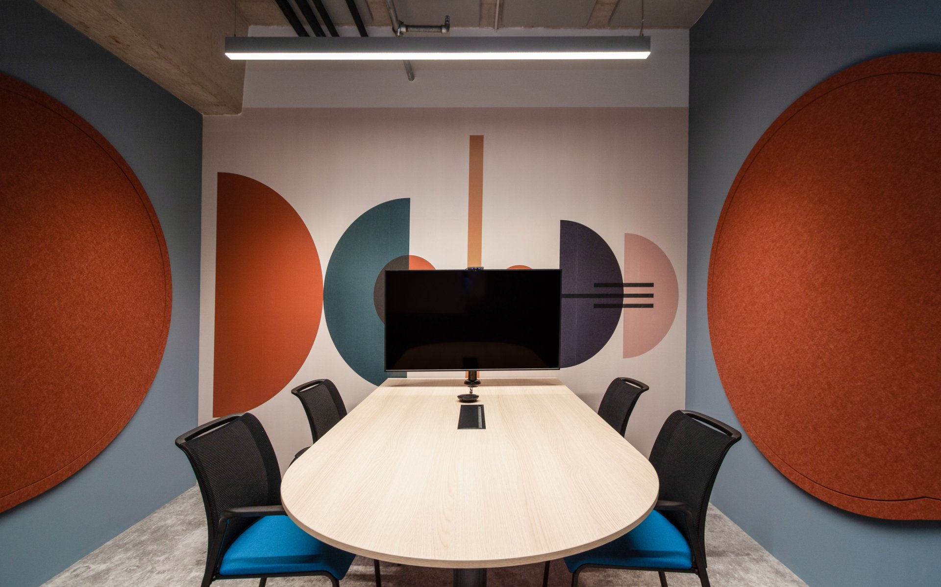 Salle de réunion de 4-5 personnes, mur avec des formes graphiques de couleur terracota et grises.