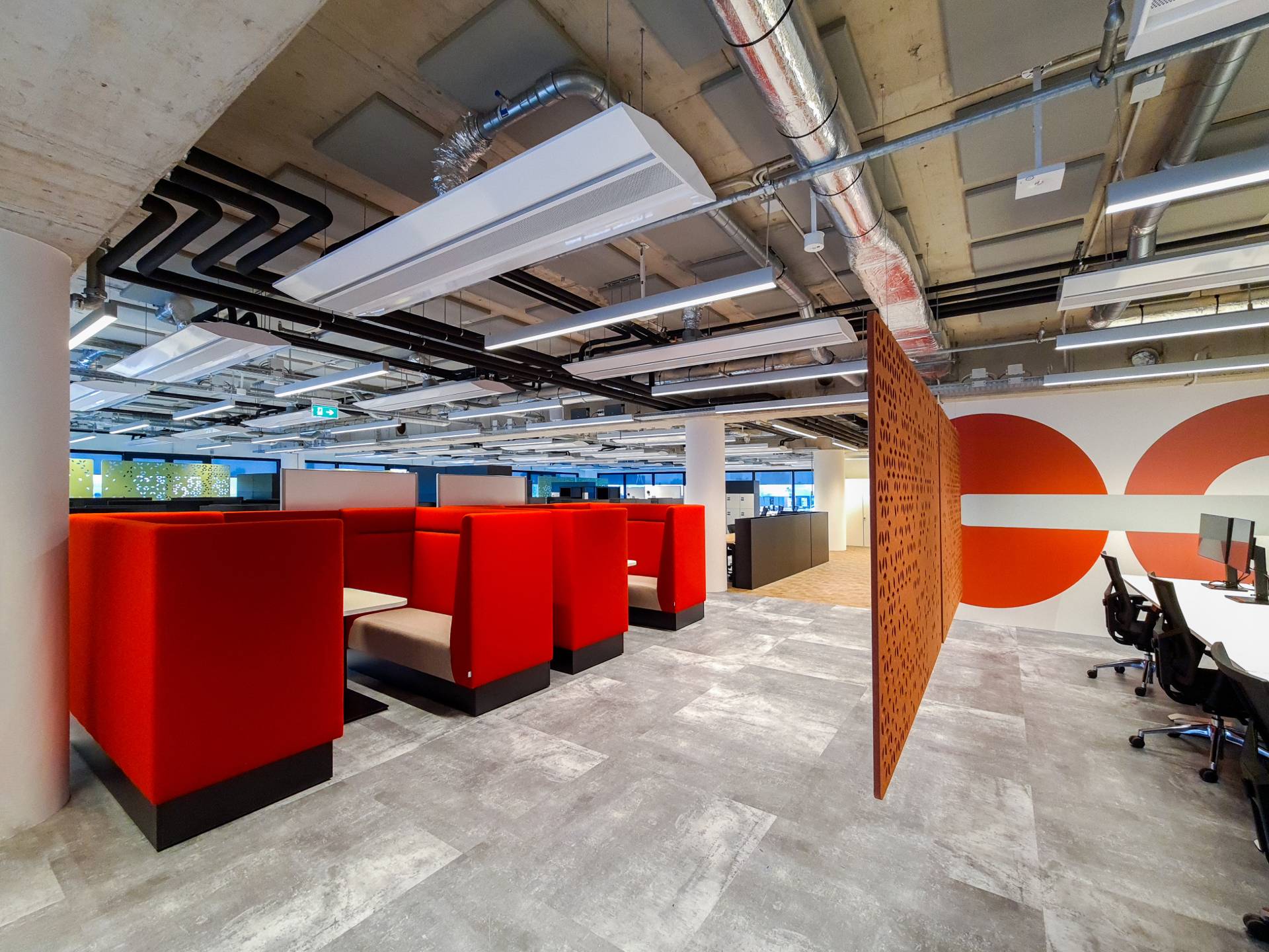 Open space avec salle de réunion semi ouverte, et petits espaces de coworking ou pour réunion informelle formé de banquettes rouges