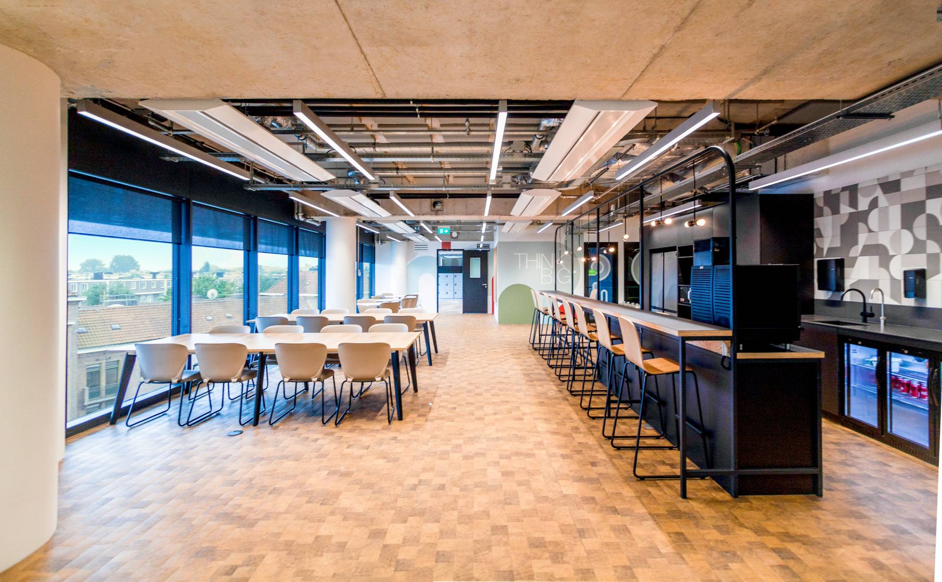 Salle de restauration, cafétéria, avec un grand bar avec chaises hautes et plusieurs tables à manger devant de grandes baies vitrées