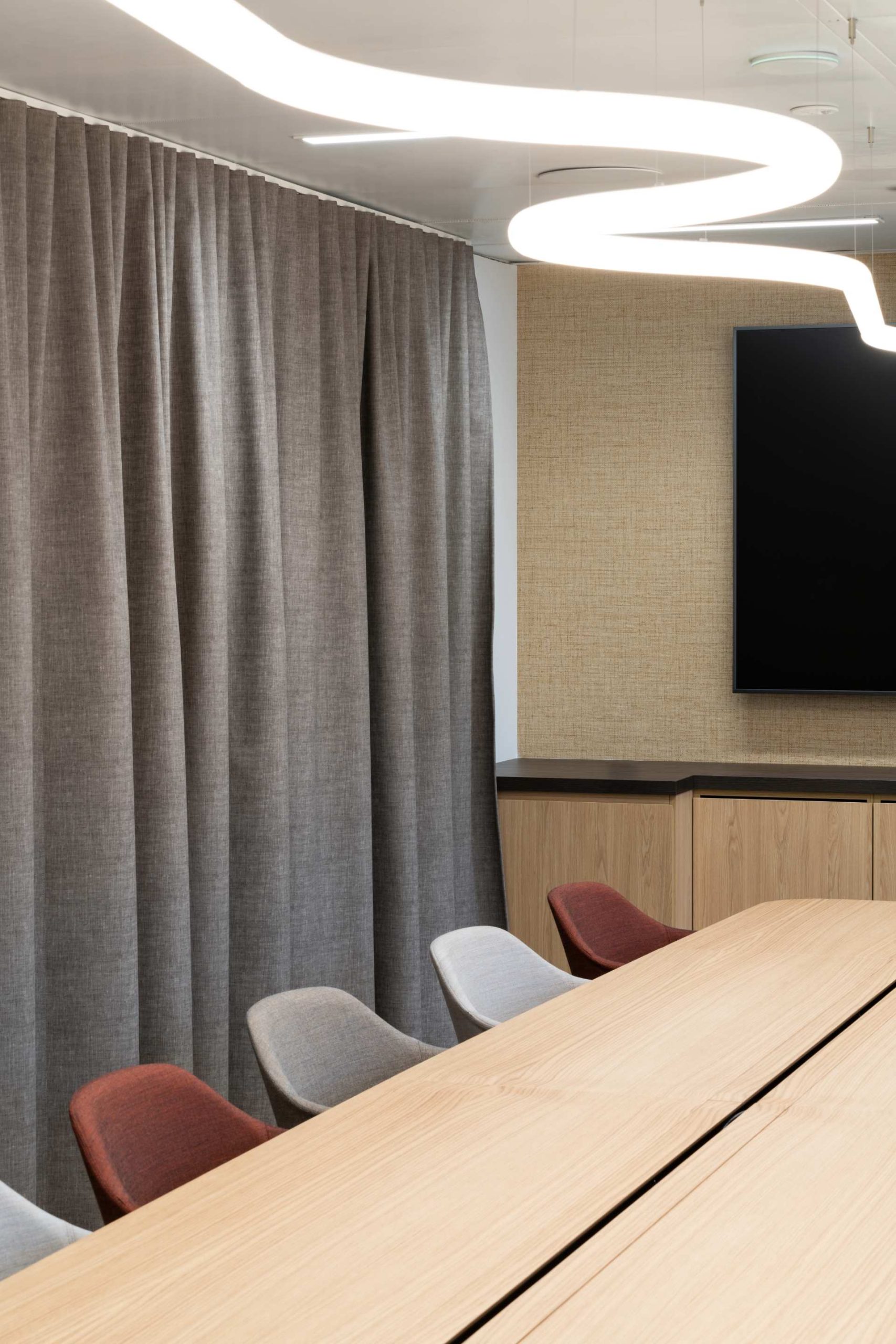 Grande salle de réunion avec un rideau pour la confidentialité, un luminaire formant une ligne qui ondule est au dessus de la grande table.