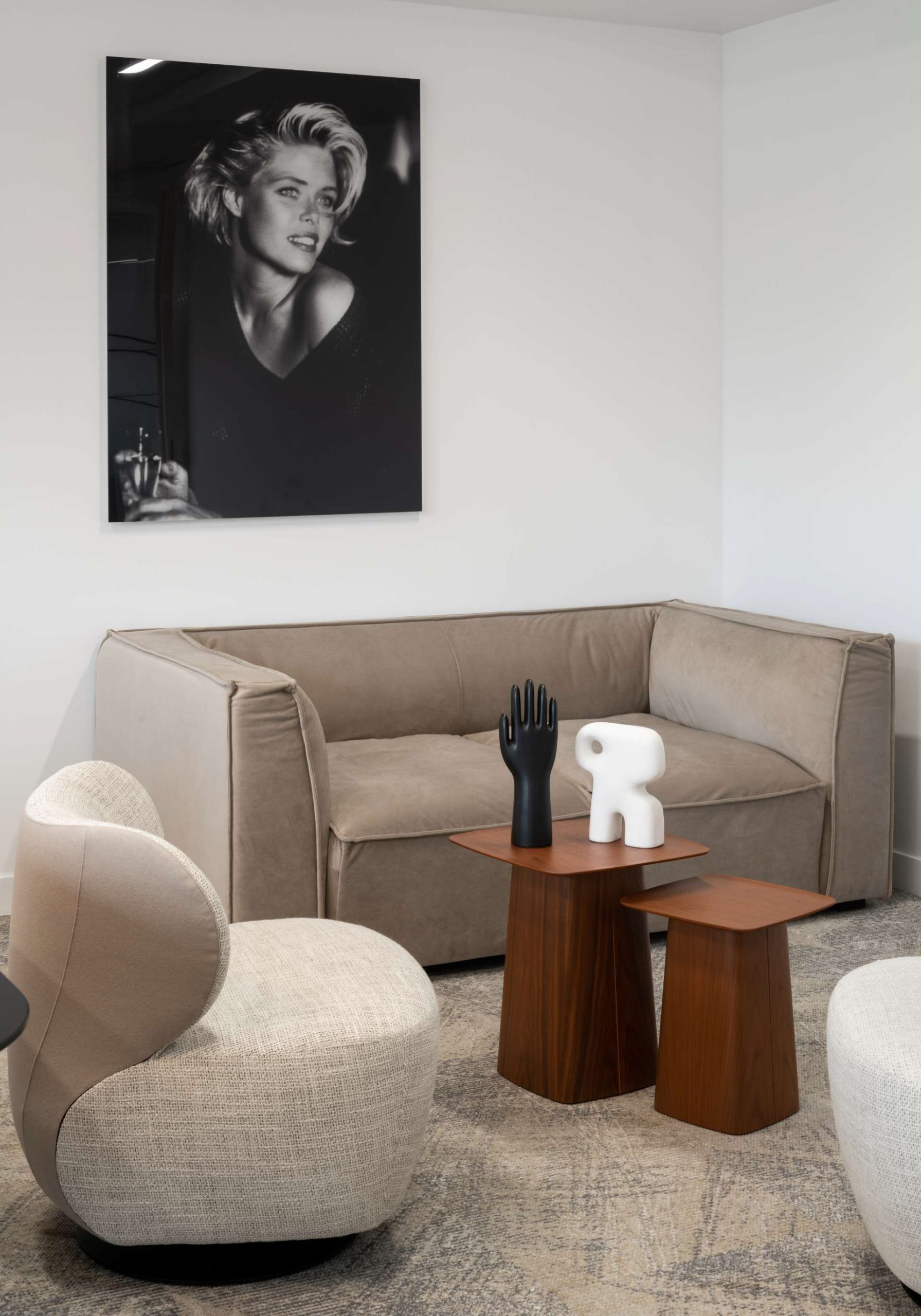 Espace cosy avec fauteuil et canapé beige et taupe. Table basse marron avec décoration dessus et photo en noir et blanc au mur derrière le canapé