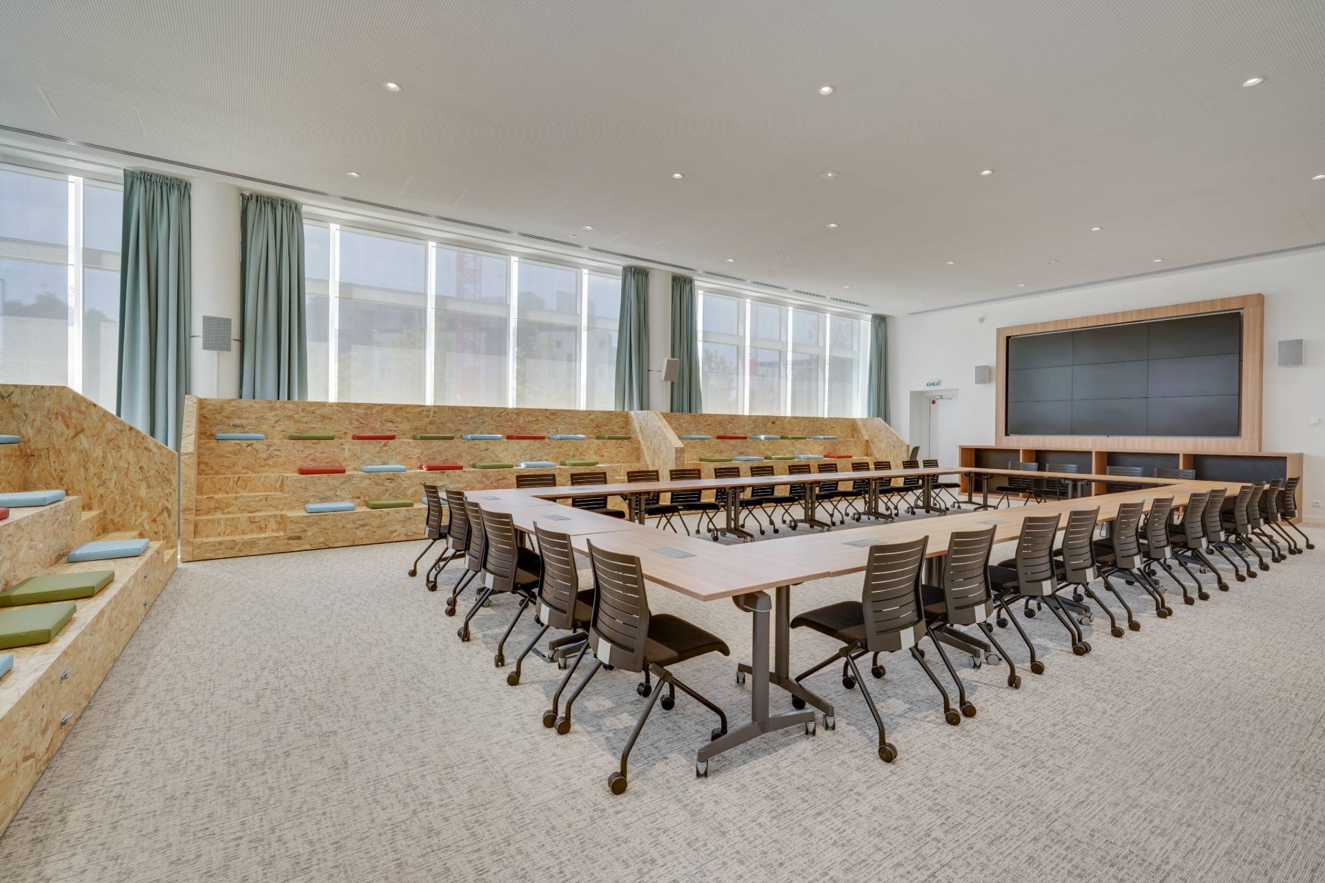 Salle de réunion avec table en U au centre et des gradins sur les côtés avec des coussins de couleurs pour les assises