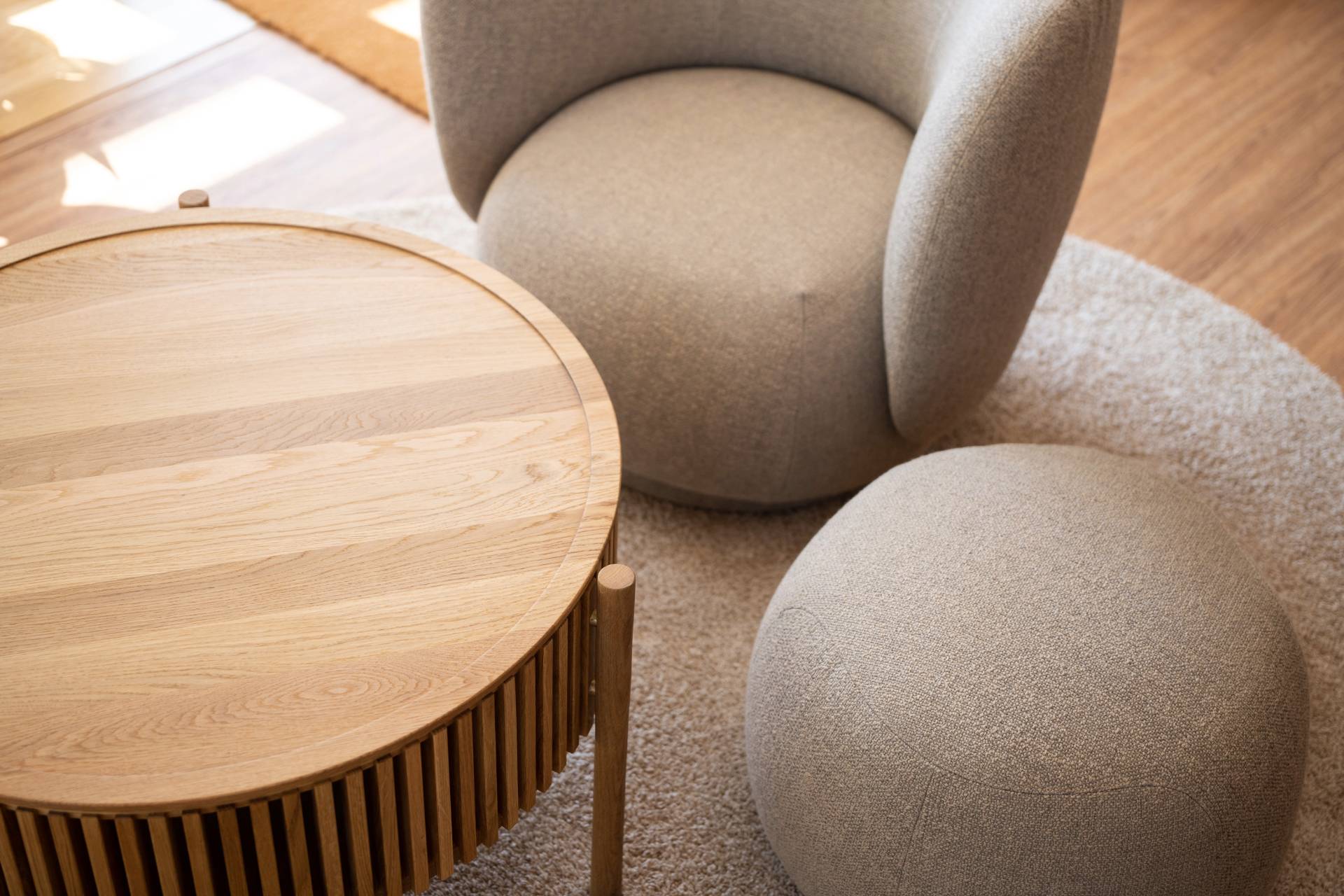 Gros plan sur table basse en bois et fauteuils et pouf en tissus gris beige clair