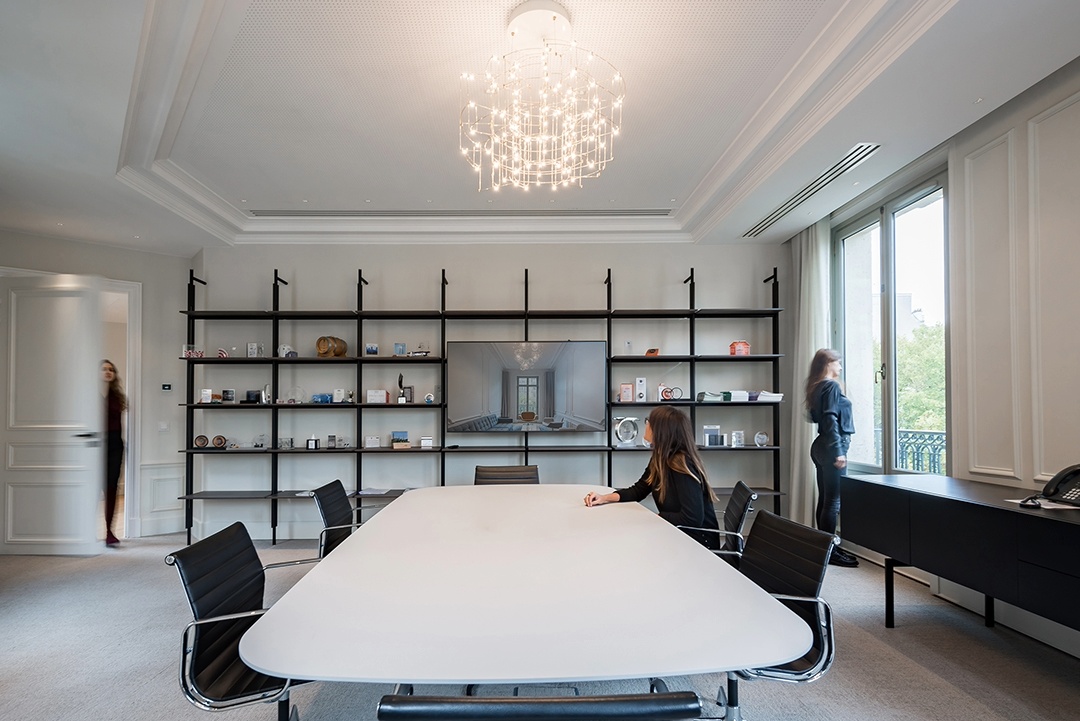 Salle de réunion avec grande table blanche, étagère sur tout le mur du fond en bois foncé, mur blanc