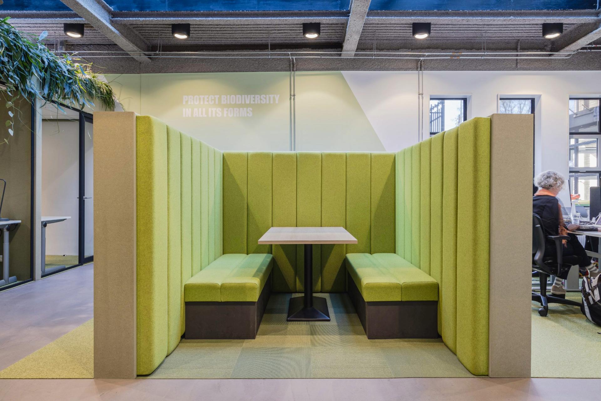 Espace de réunion informelle ouvert, avec banquette verte claire et table en bois