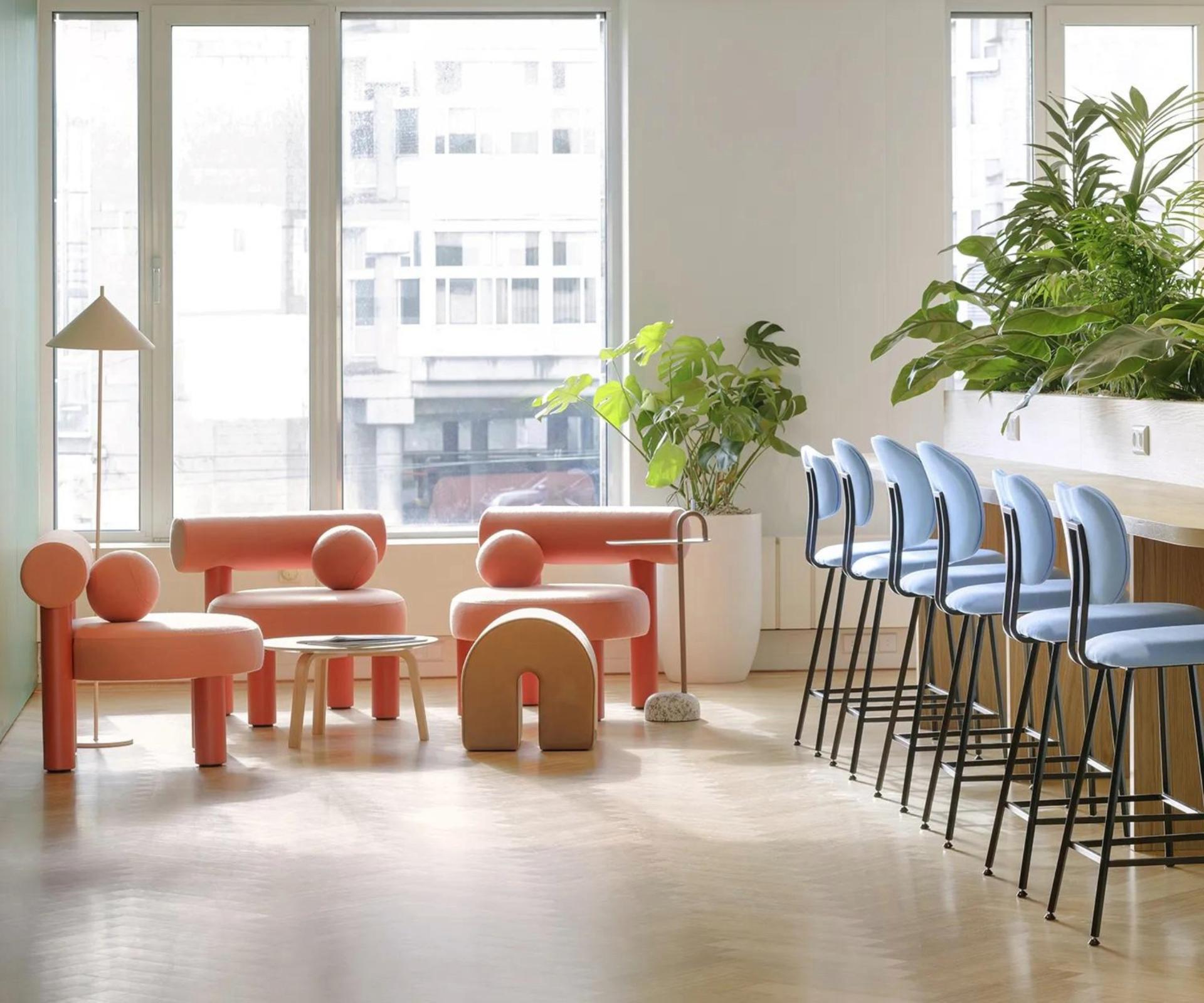 Espace cafétéria, détente, bar haut avec chaise haute bleu clair et espace cosy avec fauteuil couleur corail orangé.
