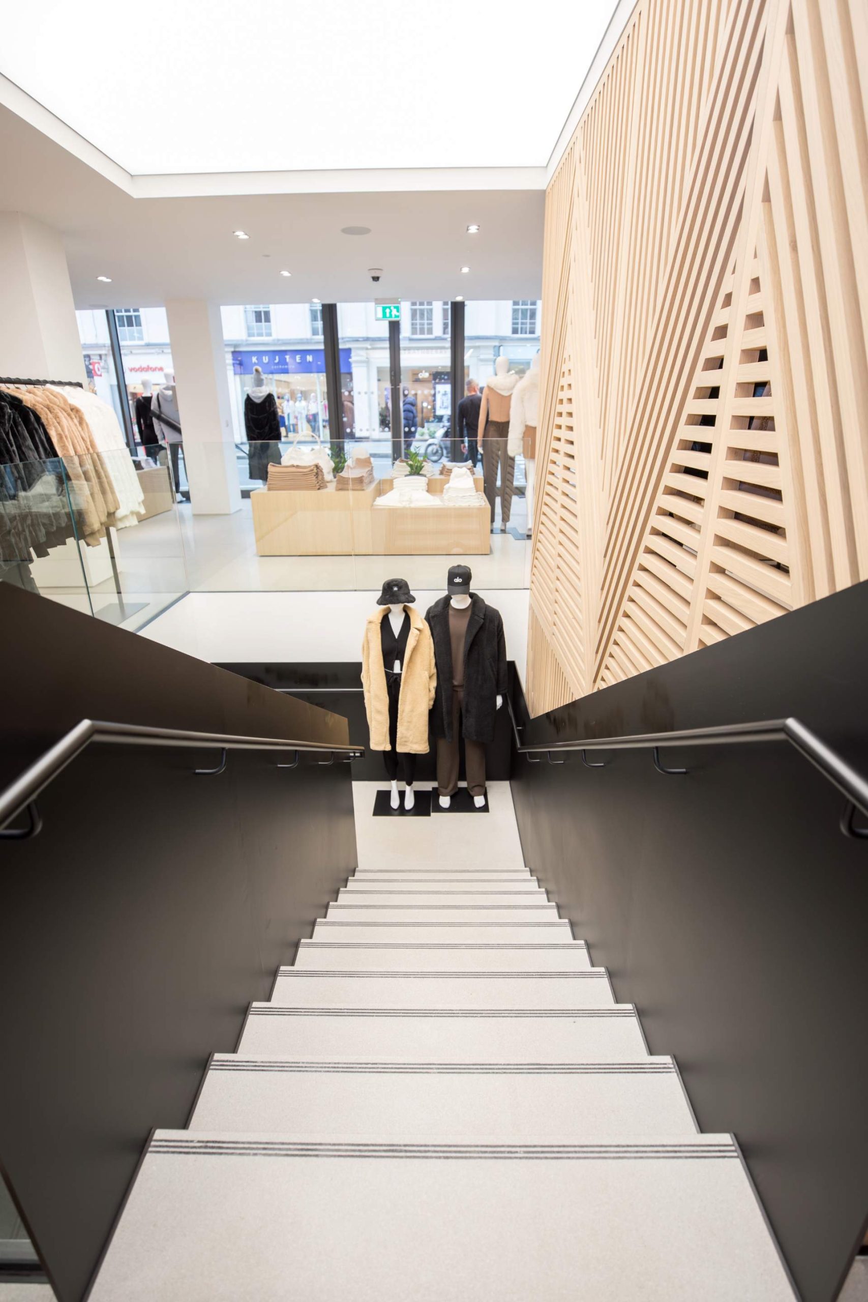 Vu du haut des escaliers, mannequins en bas, structure décorative en bois sur la droite