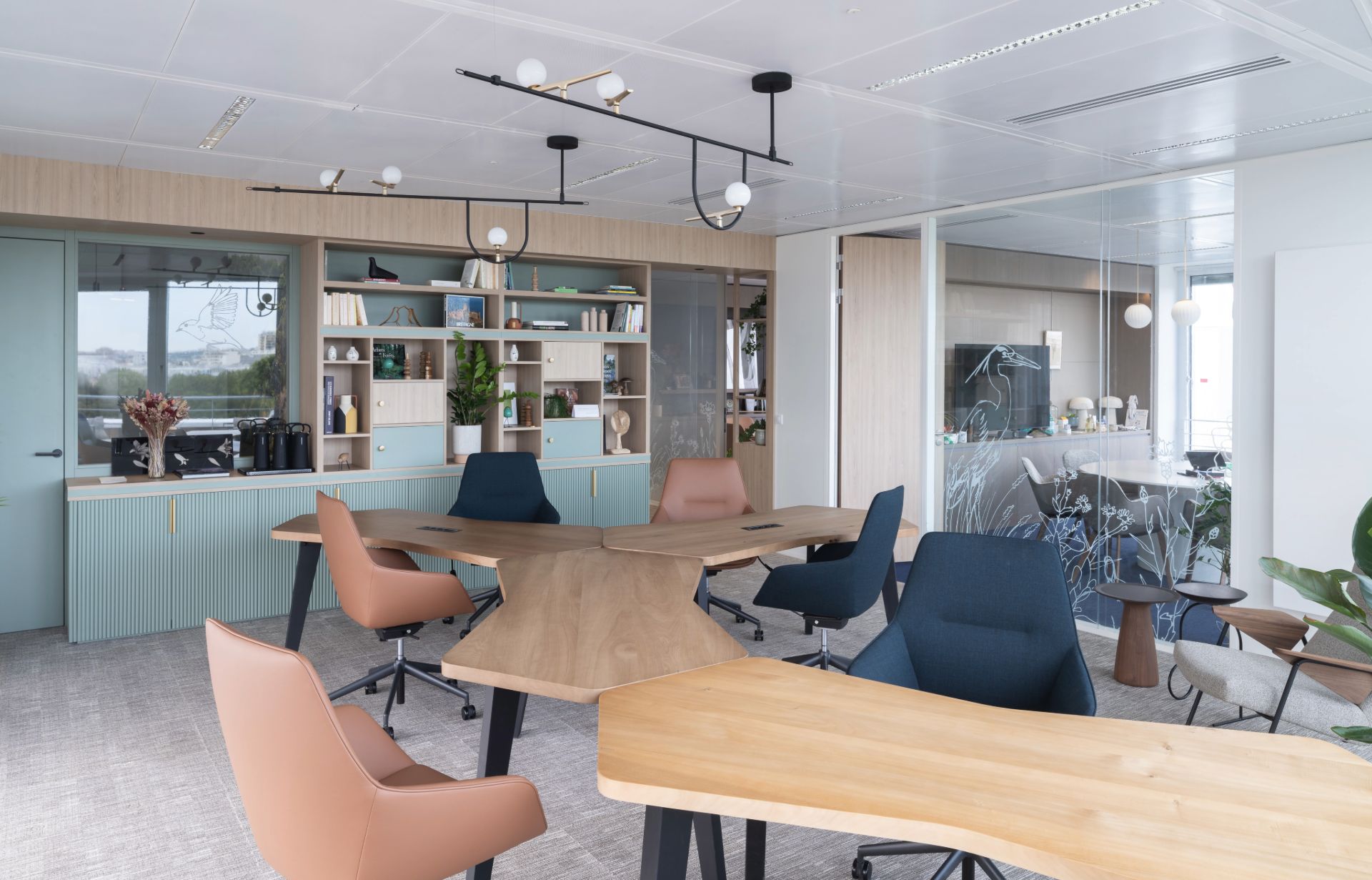 Open space ou espace de coworking, avec bureaux asymétriques en bois clair et chaises bleues ou vieux rose