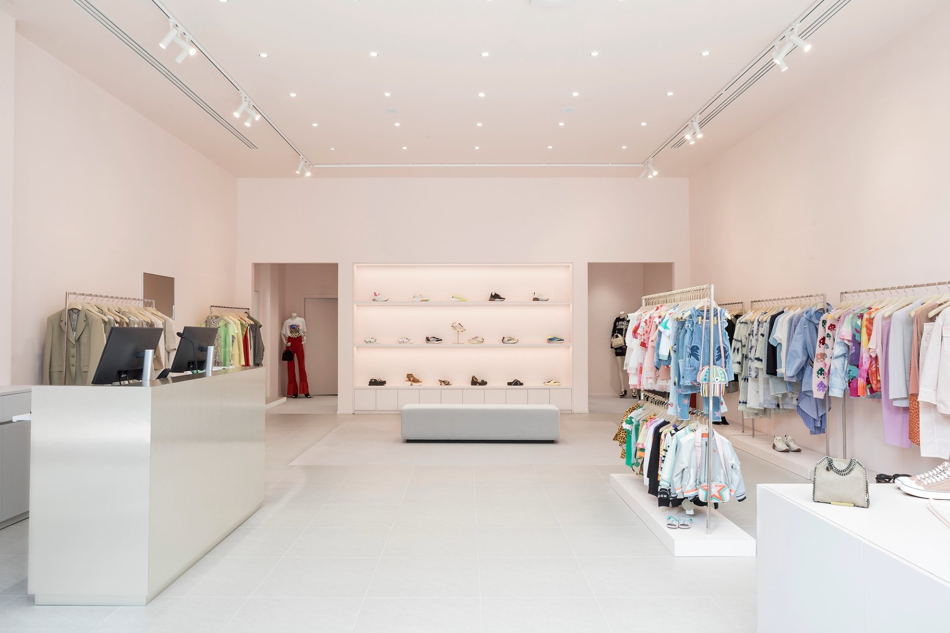 Vue de l'ensemble du magasin, murs rose pâle, des vêtements sur la droite et des chaussures et accessoires dans le fond