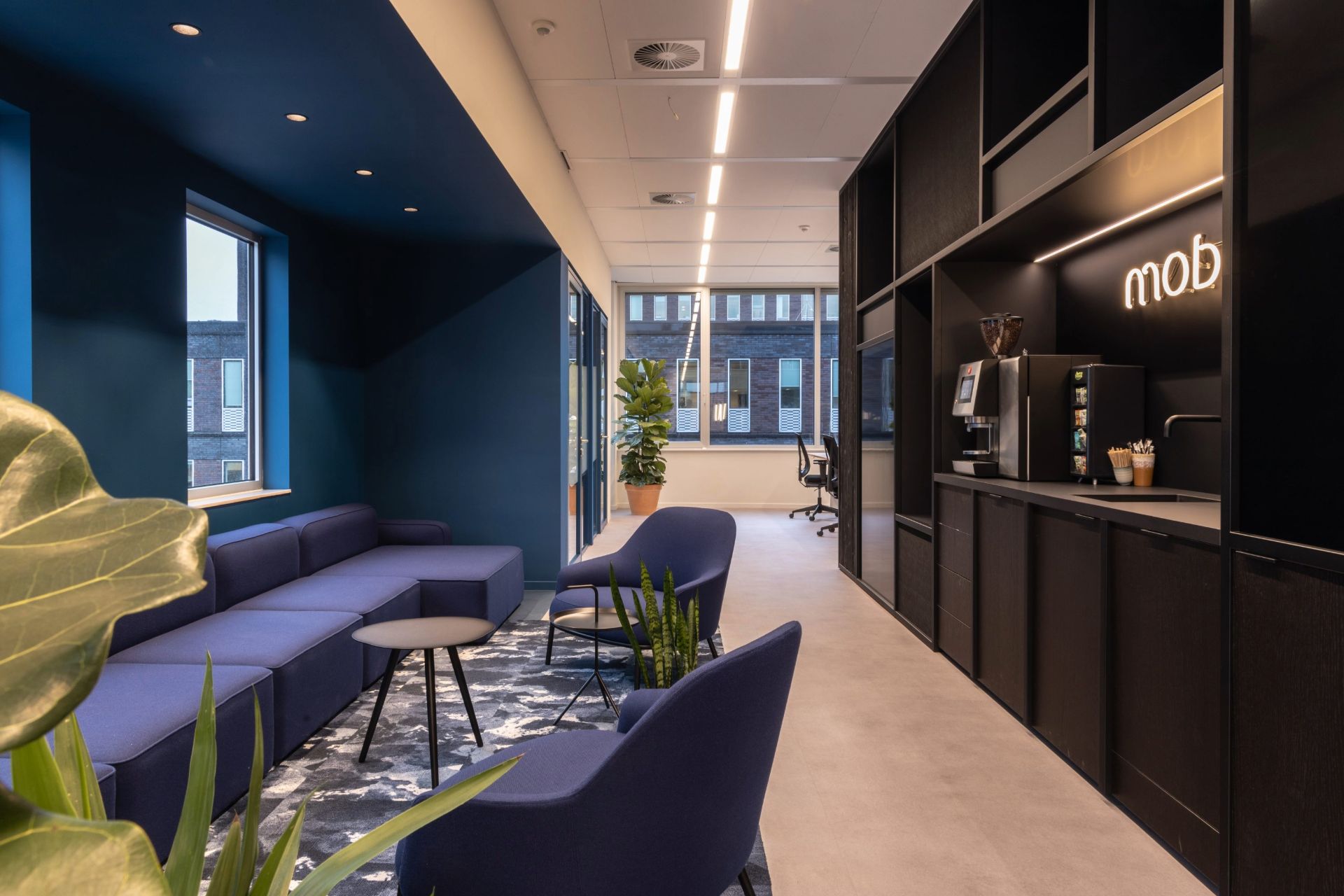Espace cafétéria avec meubles noirs, en face d'une grande banquette dans une alcôve bleue