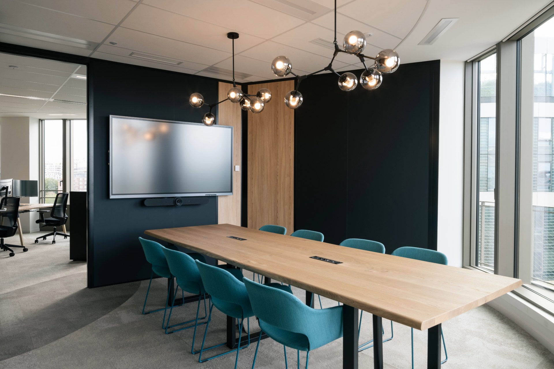 Salle de réunion semi ouverte, avec grande table en bois clair et sièges bleu canard