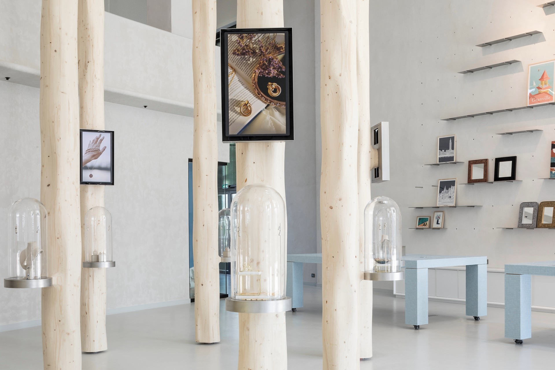 Oeuvres exposées sous des cloches accrochées à des poteaux de bois, avec tableau au dessus - Maison des métiers d'art