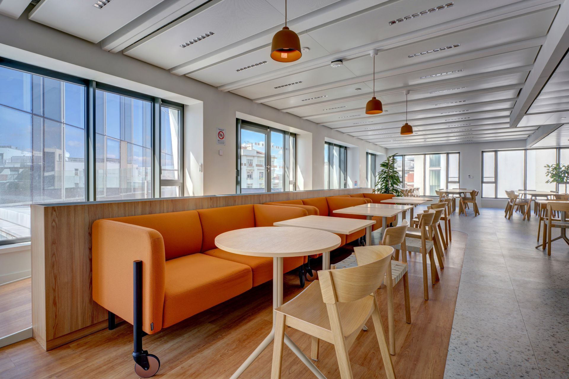 Salle de restauration avec assises de couleur orange et tables et chaises en bois clair. Chez NAOS par Parella