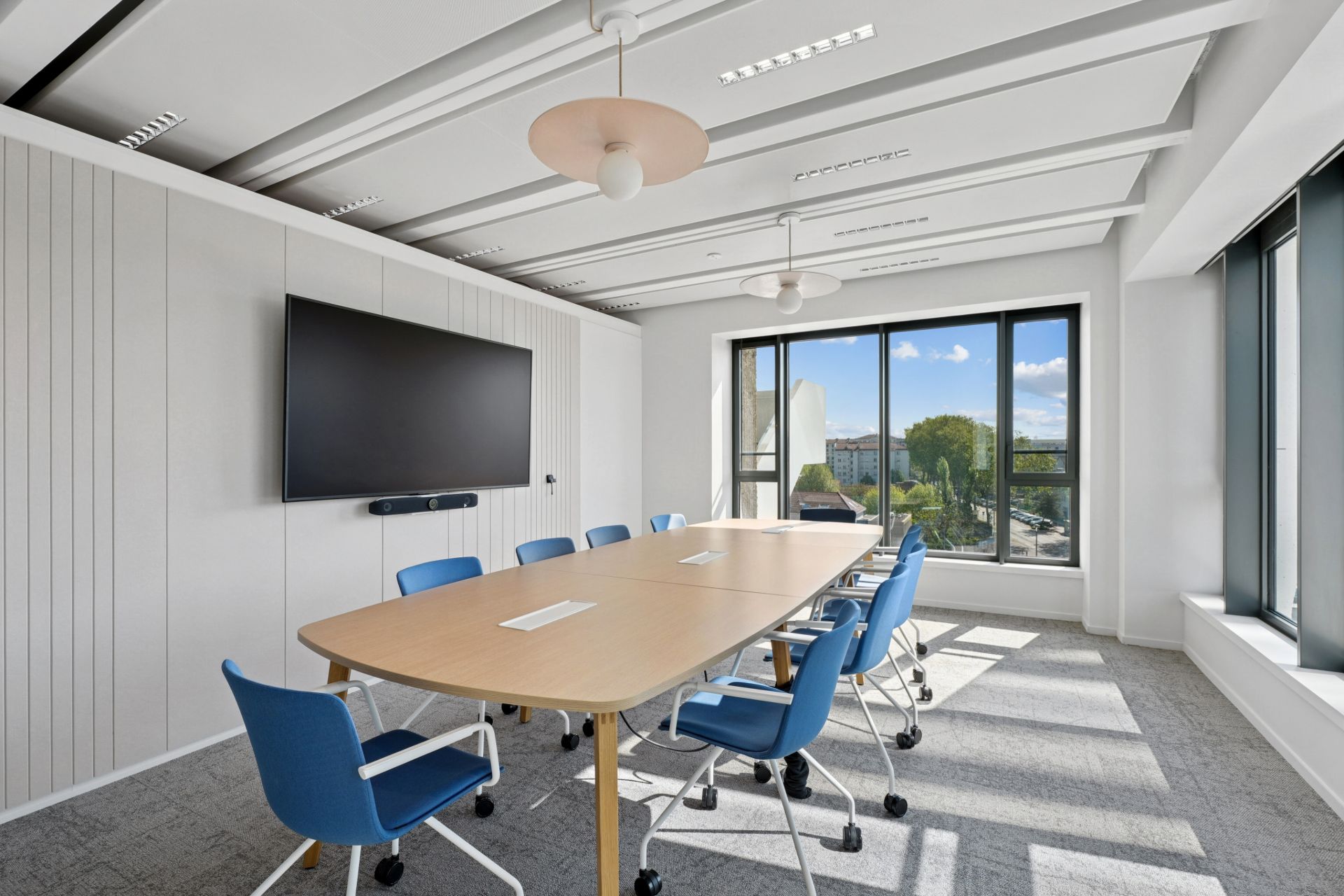 Salle de réunion avec grande table en bois clair et chaises bleues, chez NAOS, par Parella