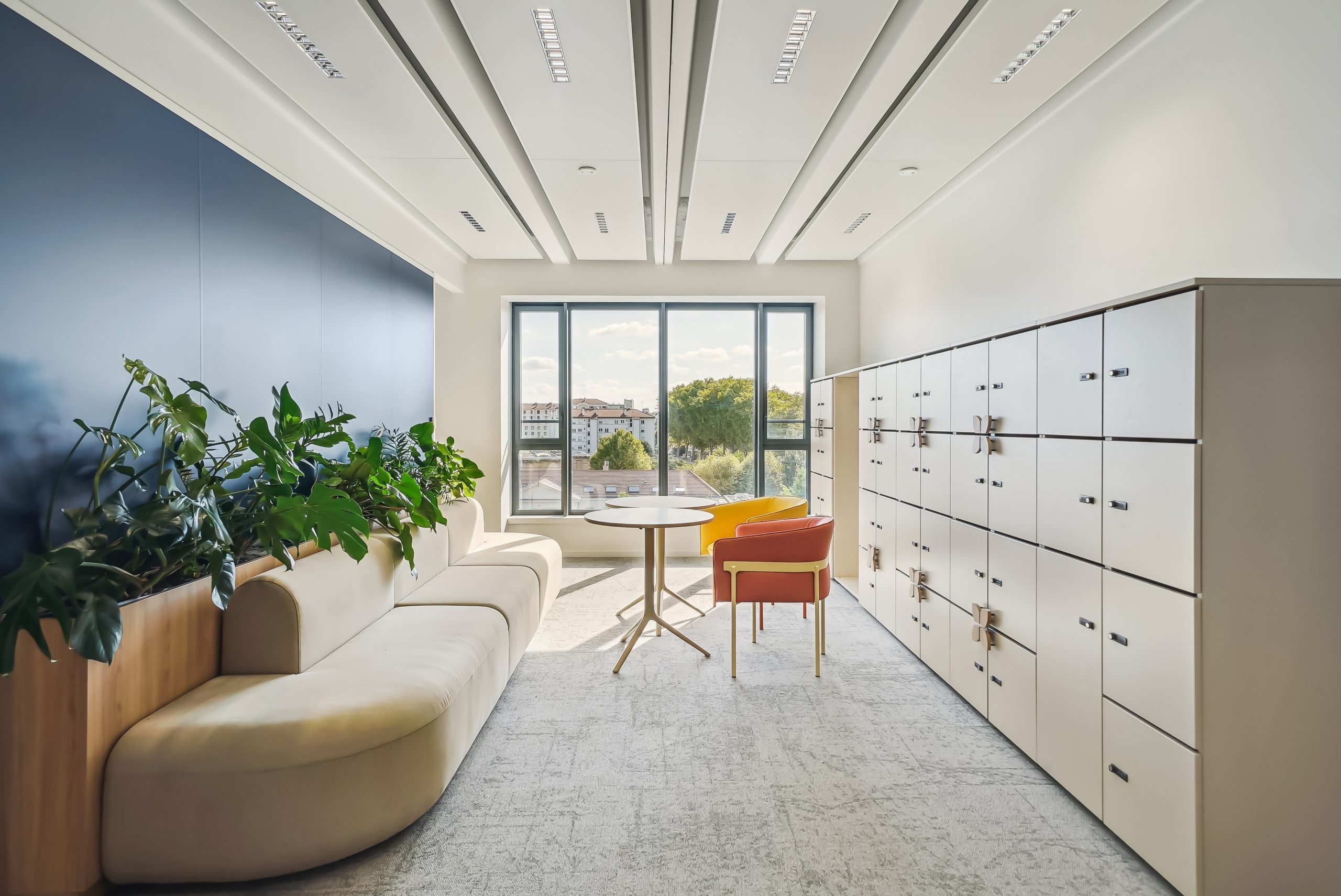 Pièce avec grande ouverture de lumière au fond, casiers, fauteuils et canapé gris.