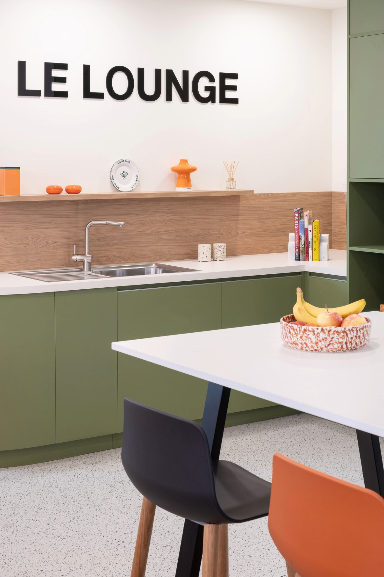 Photo d'une cuisine verte avec inscription Le Lounge et au premier plan une table et des chaises noire et orange.