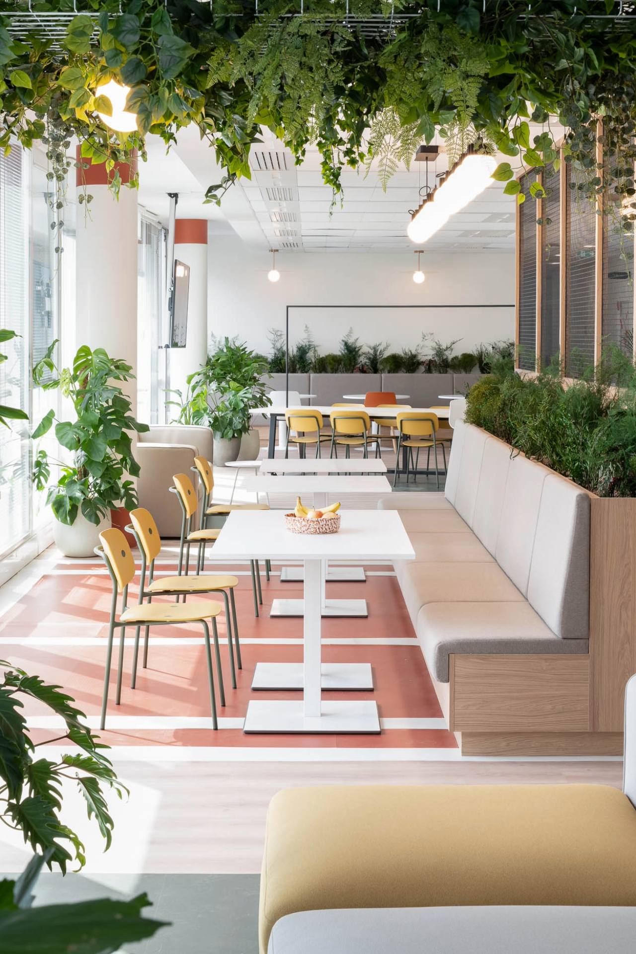 Photo d'une cafétéria avec de la végétalisation et au centre une rangée de tables avec des chaises et une banquette.
