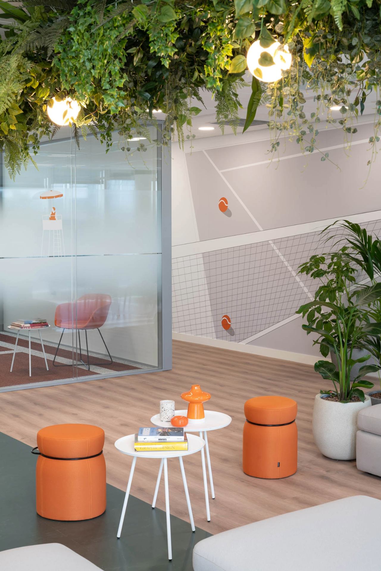 Photo espace détente avec table basse + tabourets orange et au plafond des végétaux.