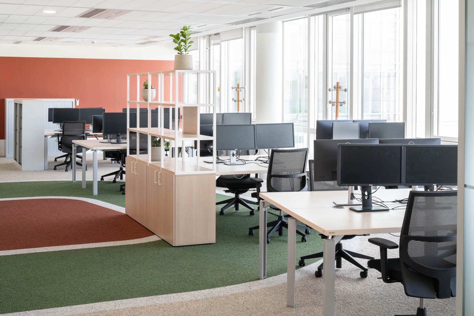 Photo d'un open space d'une rangée de bureaux avec écrans d'ordinateur et une moquette verte au sol.
