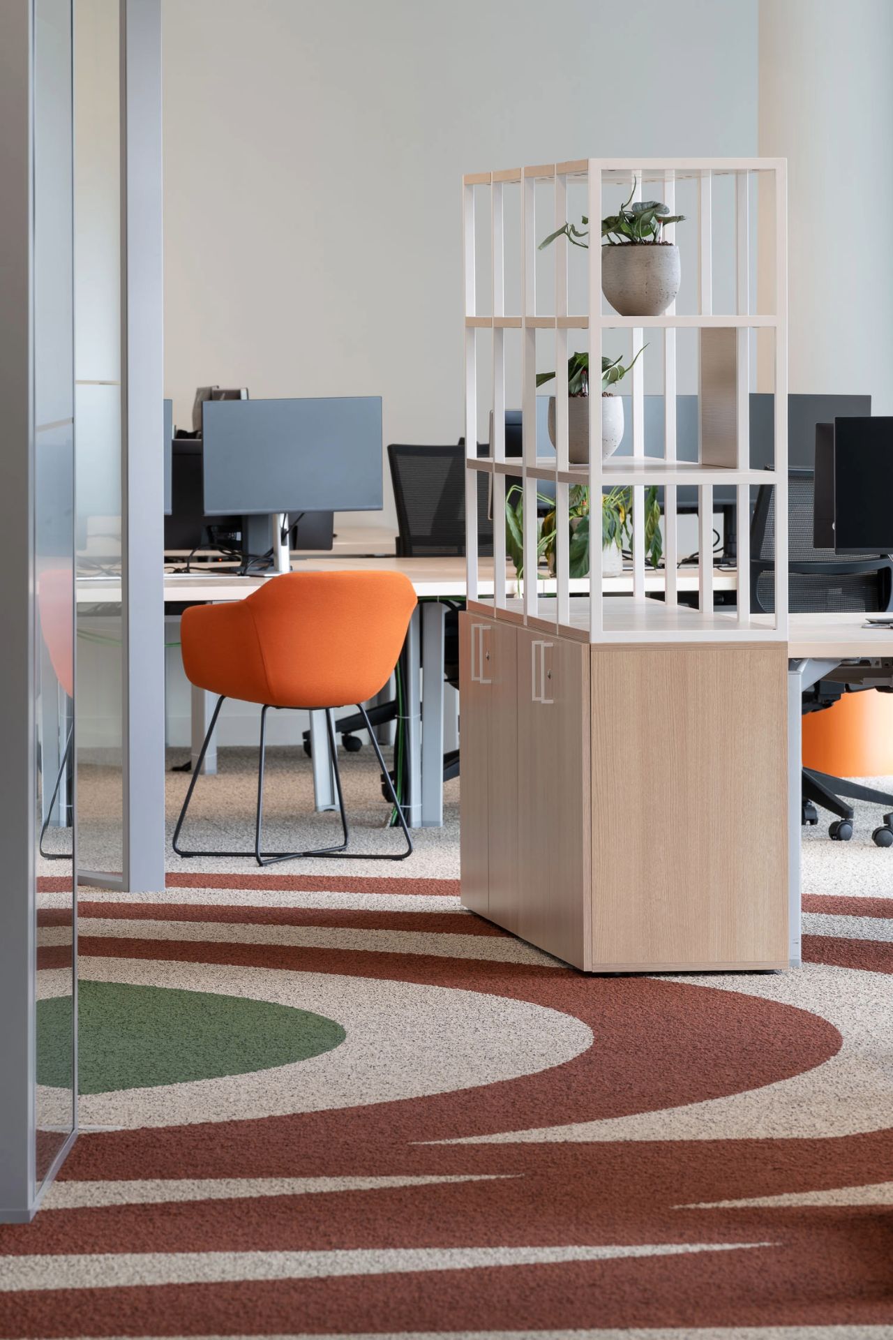 Photo d'un bureau marron clair avec chaise orange et au sol une moquette en forme de cocarde.