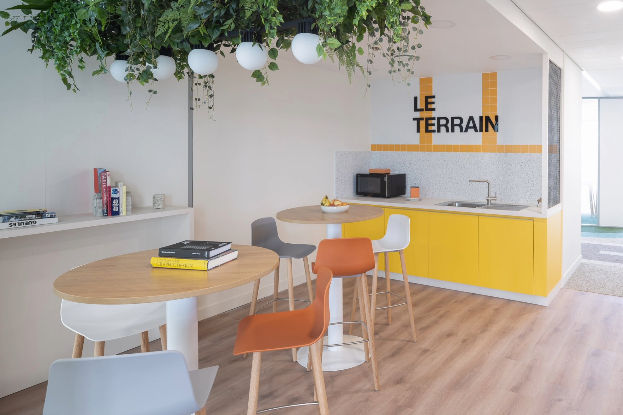 Photo d'un espace convivial avec cuisine jaune et inscription Le Terrain plus un livre posé sur une table au premier plan.