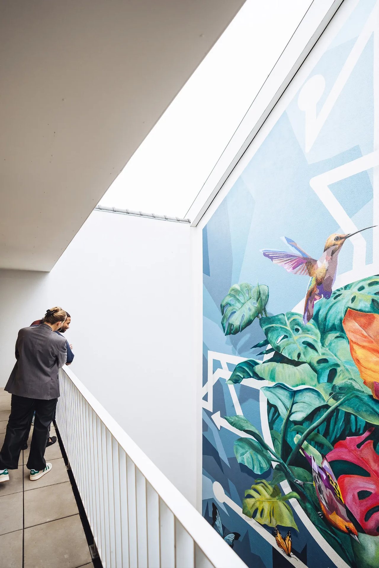 Deux personnes regardant une fresque murale à droite représentant un oiseau et des fleurs.