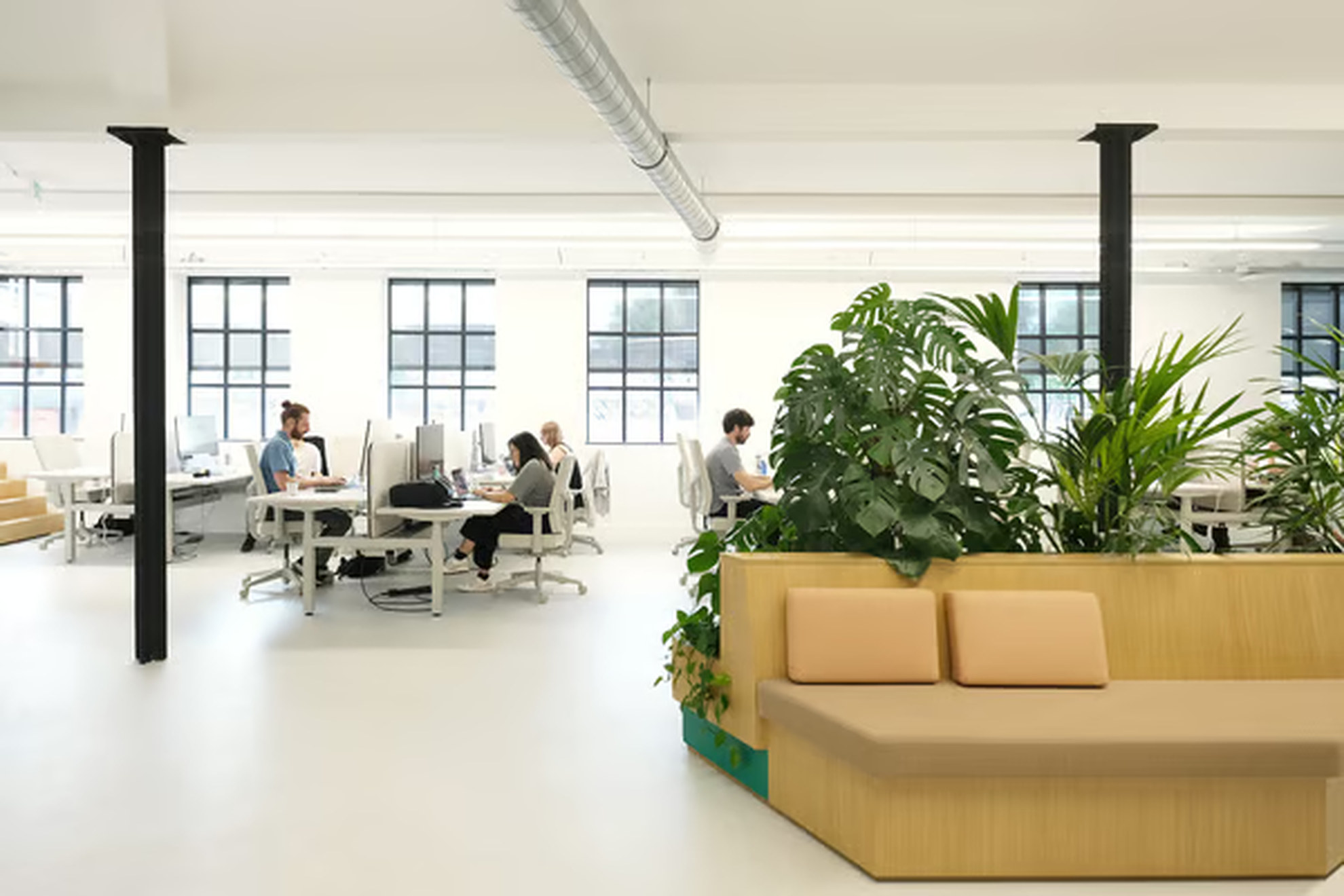 Banquette avec des végétaux + posts de bureaux avec une rangée de fenêtres rectangulaires.