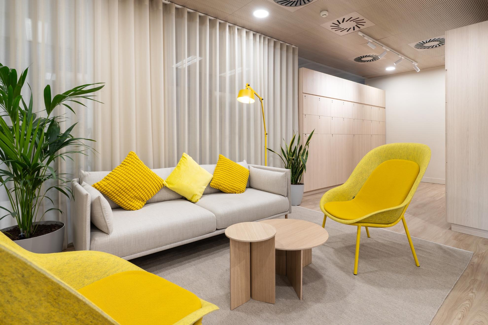 Canapé gris avec coussins jaunes et des chaises jaunes plus deux tables basses en bois.