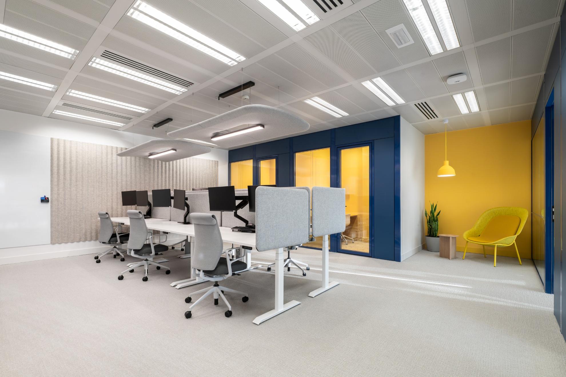 Postes de travail gris avec des salles de réunions jaunes et une façade bleue.