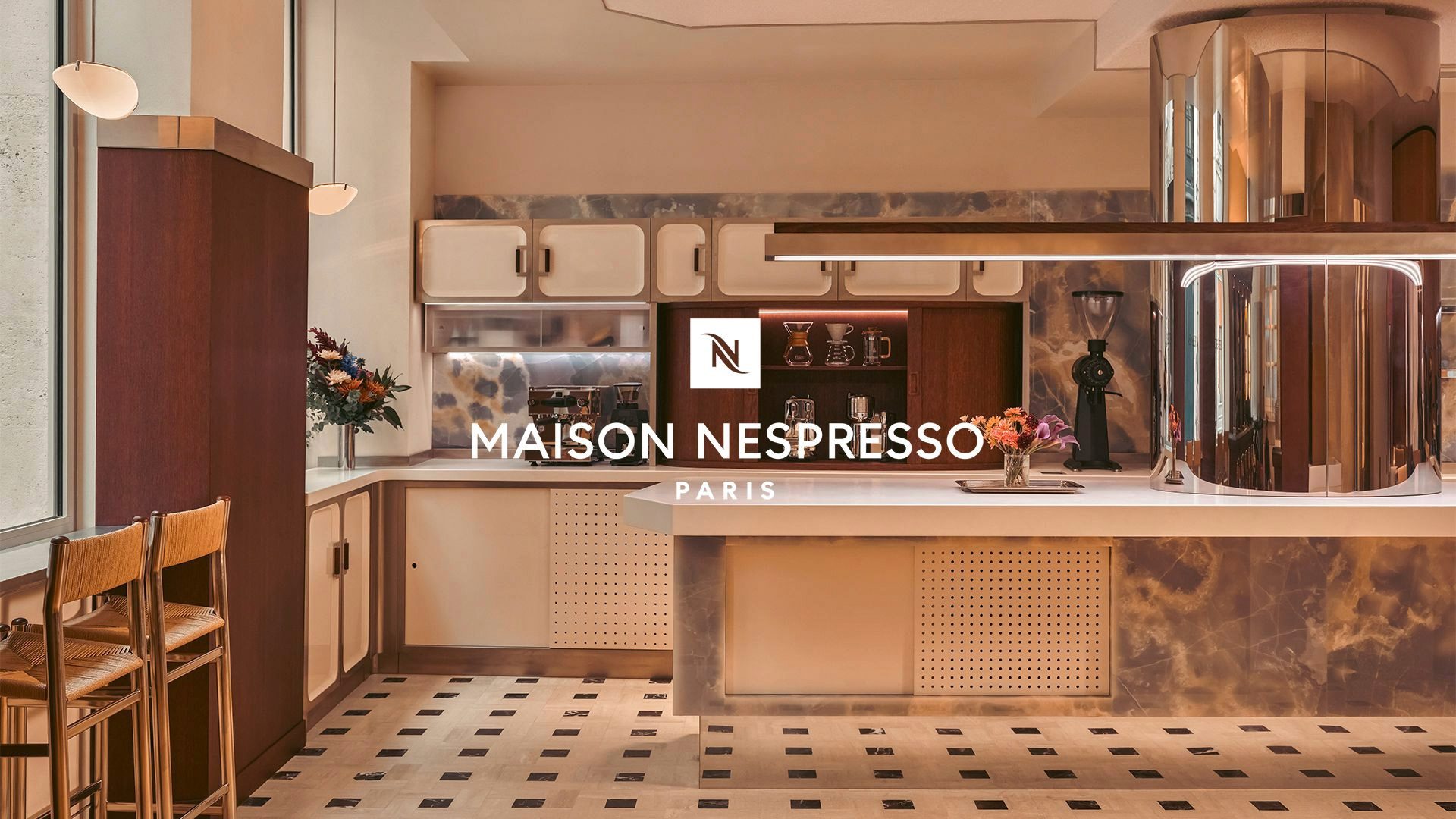 Comptoir au centre avec armoire à gauche et deux chaises + une cuisine au fond.