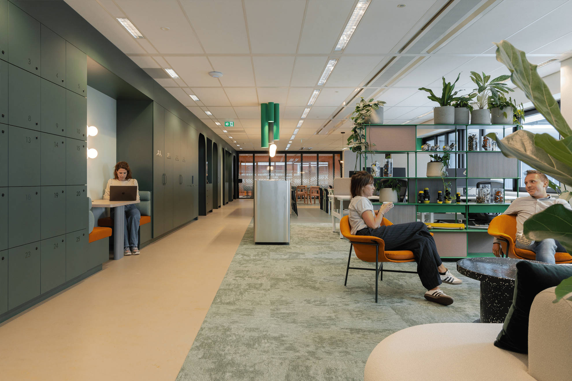 Un espace ouvert avec à gauche des banquettes pour travailler et à droite un espace détente avec des chaises + une étagère de végétaux.