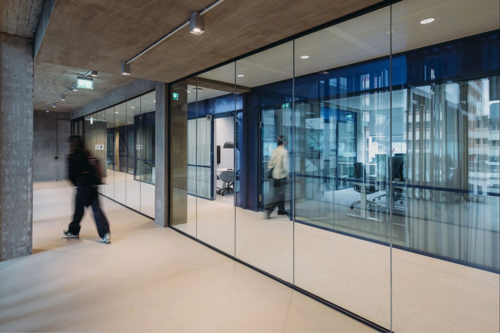 Vue sur un mur en mirroir avec un pilier et plafond en format brut avec deux personnes visibles sur la photo.