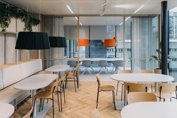Salle de restauration avec des tables et des chaises plus en arrière-plan une salle de réunion avec deux lampes orange.