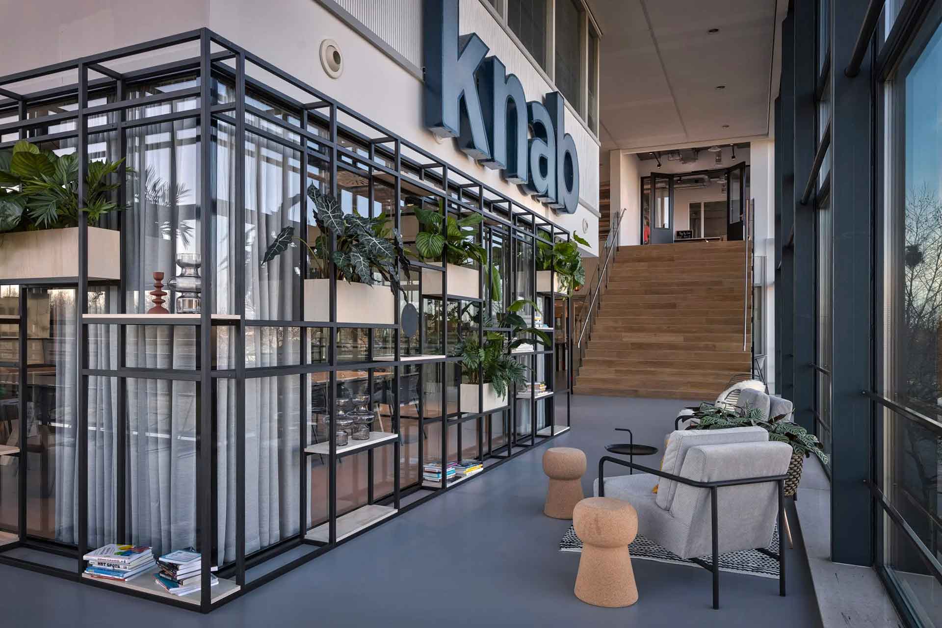 Photo d'une allée de bureau, à gauhce un etagere avec des pots de fleurs, le logo Knab est au dessus, au fond un escalier