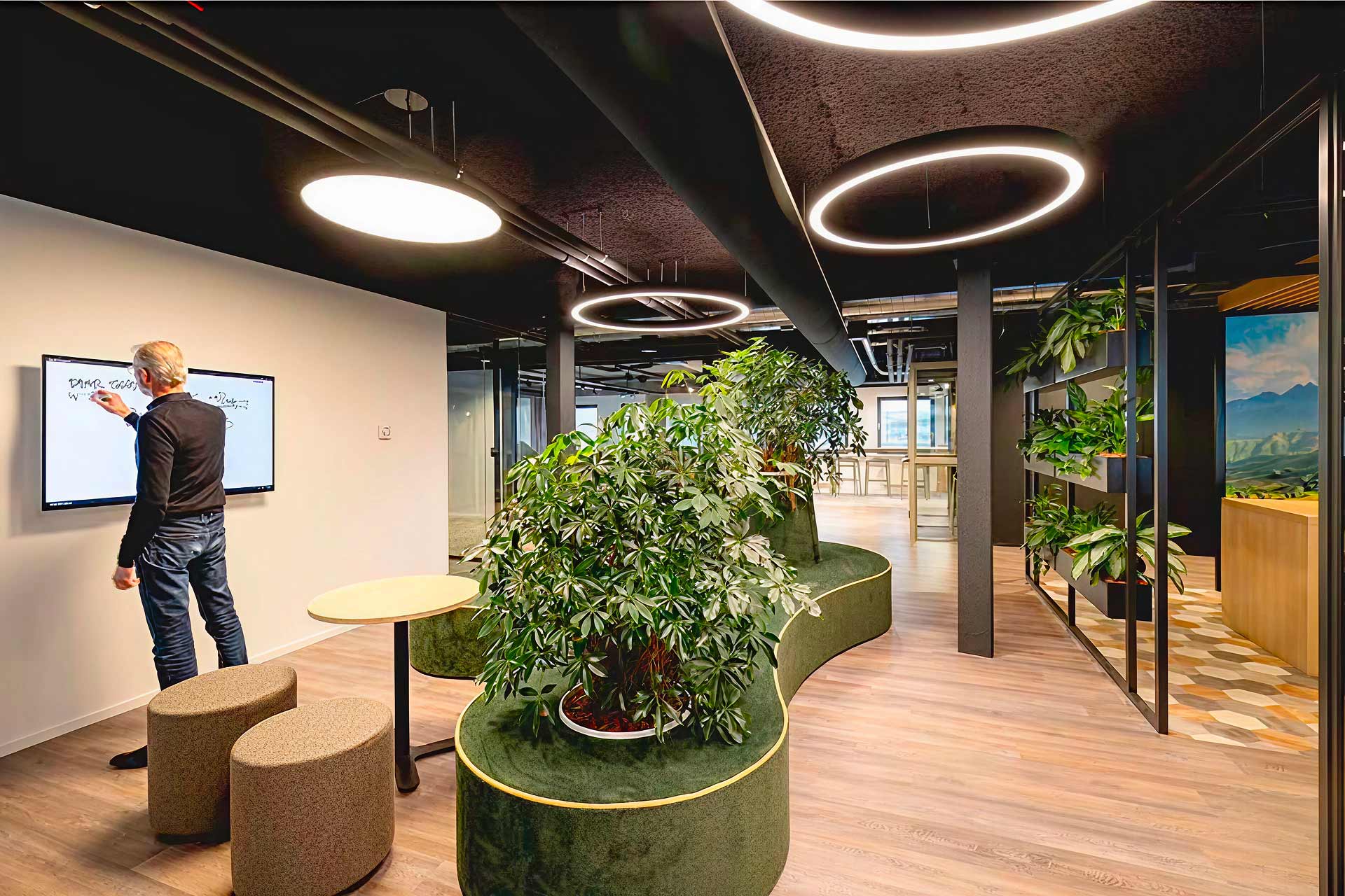 Photo d'un bureau avec au centre un parterre de plante, à gauche un homme qui écrit sur un tableau