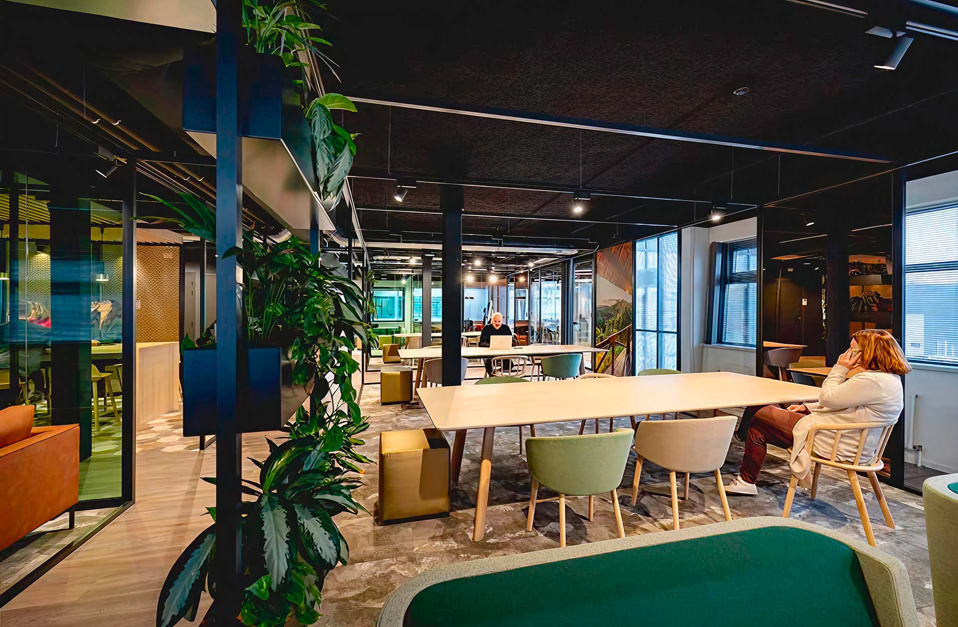 Photo d'un open-space avec à droite des tables longues avec une femme assise au telephone