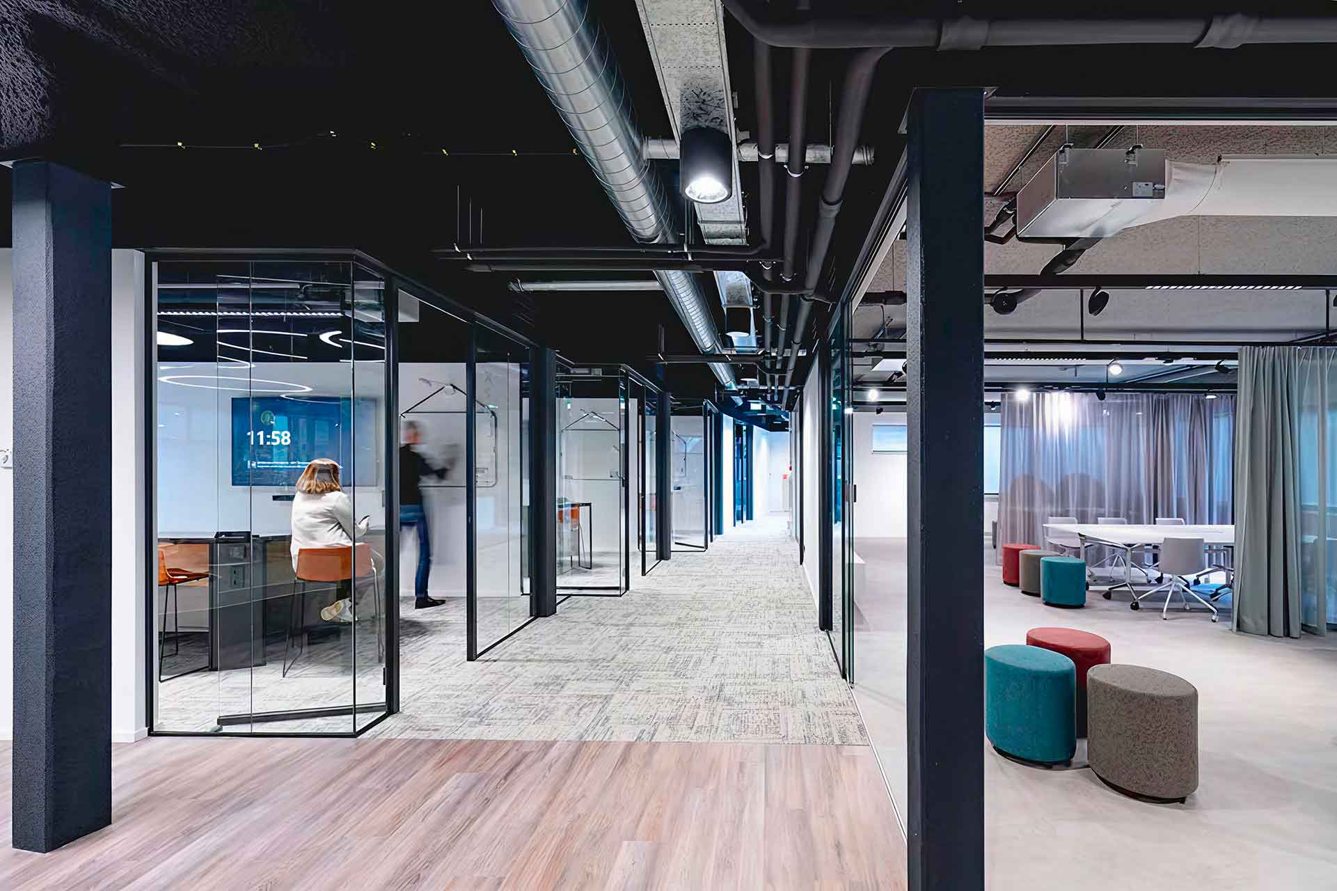 Photo d'une allée de bureau avec à gauche une salle vitrée et deux personne dedans et à droite une salle ouverte