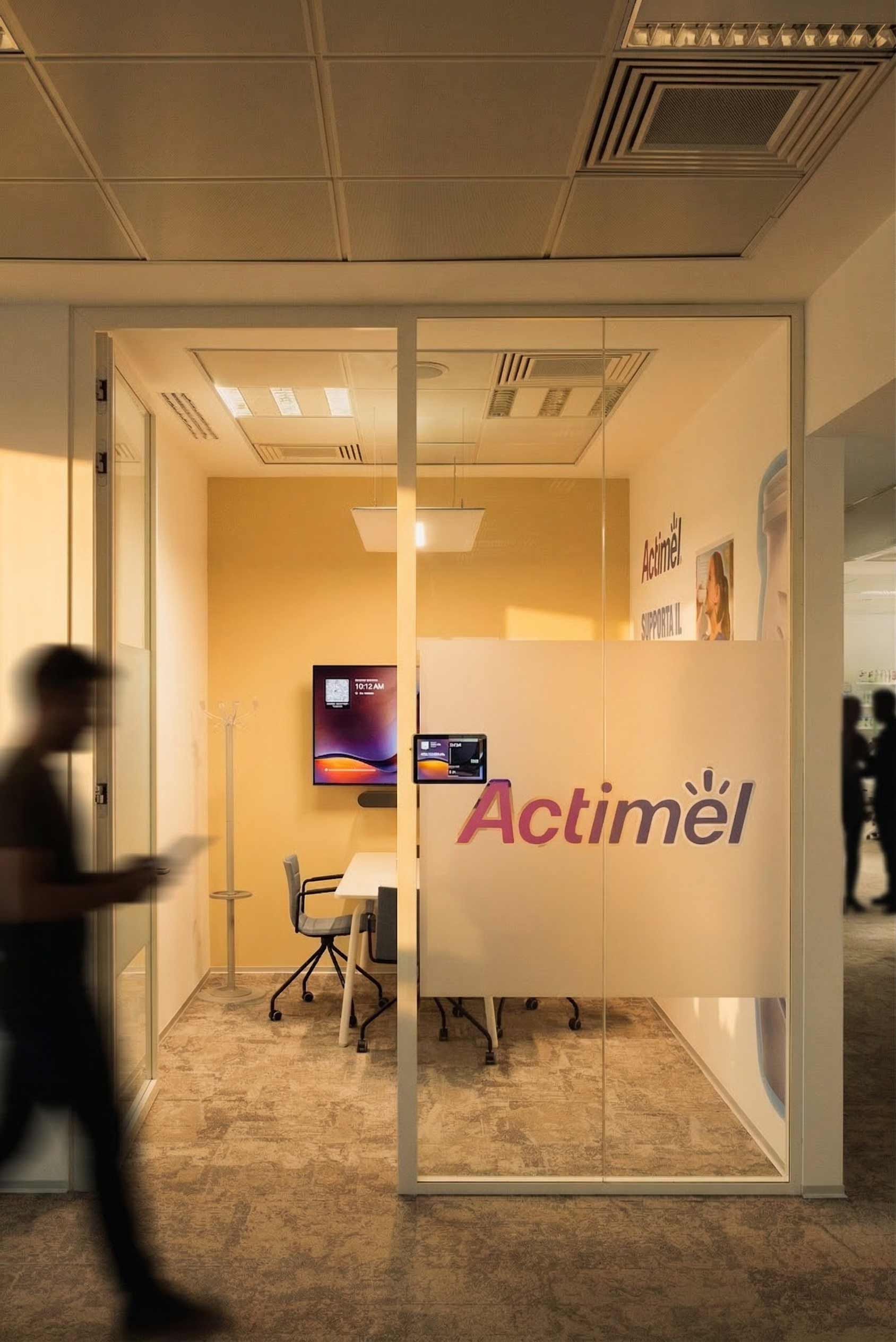 Un focus sur une petite salle de réunion vitrée dédiée à la marque Actimel, équipée d'un écran et d'une table de travail.