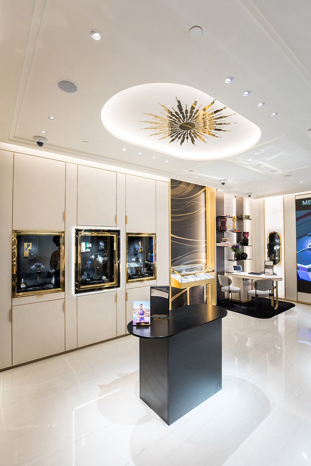 Une vue d'ensemble de la boutique montrant un comptoir central noir, des vitrines murales intégrées et un luminaire sculptural doré au plafond.