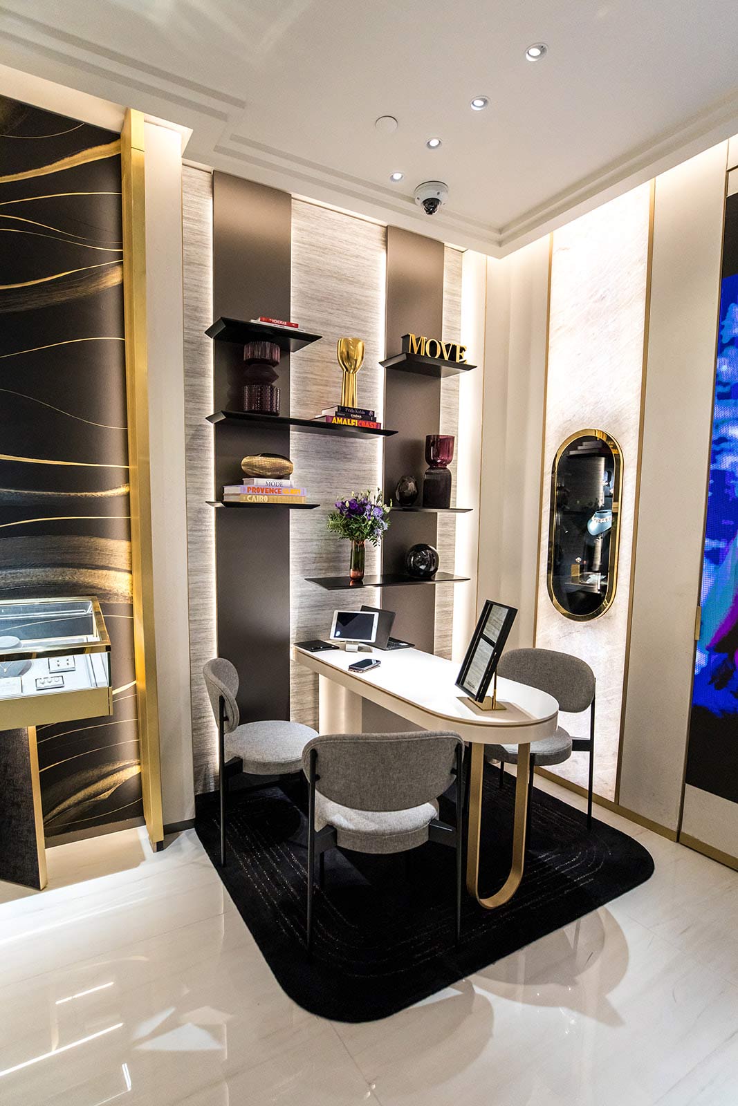 Un espace de consultation élégant composé d'une table blanche courbée, de chaises grises modernes et d'étagères décoratives rétroéclairées.