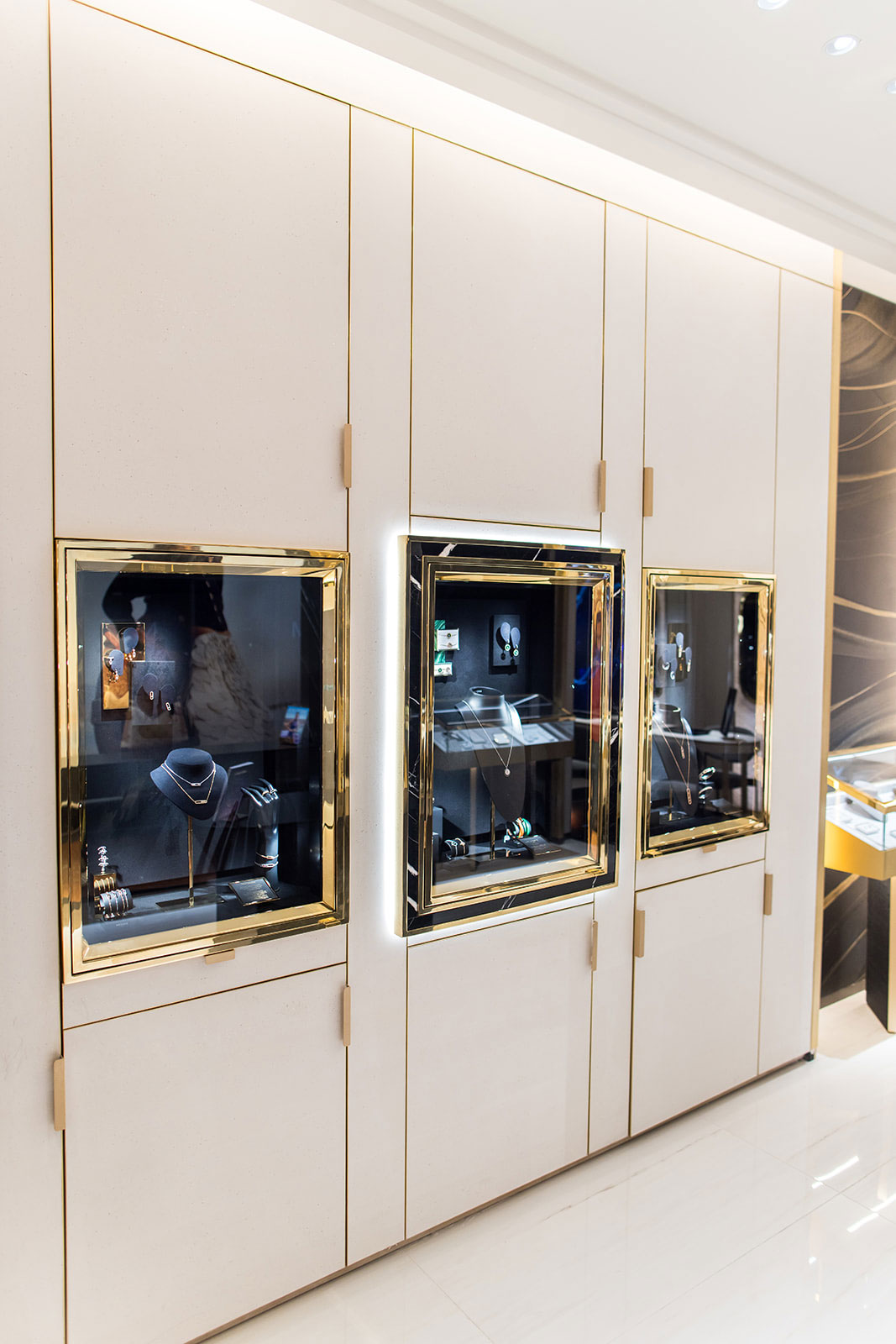 Un détail des vitrines encastrées dans des murs crème, encadrées de laiton doré et de marbre noir pour présenter les colliers et bracelets.