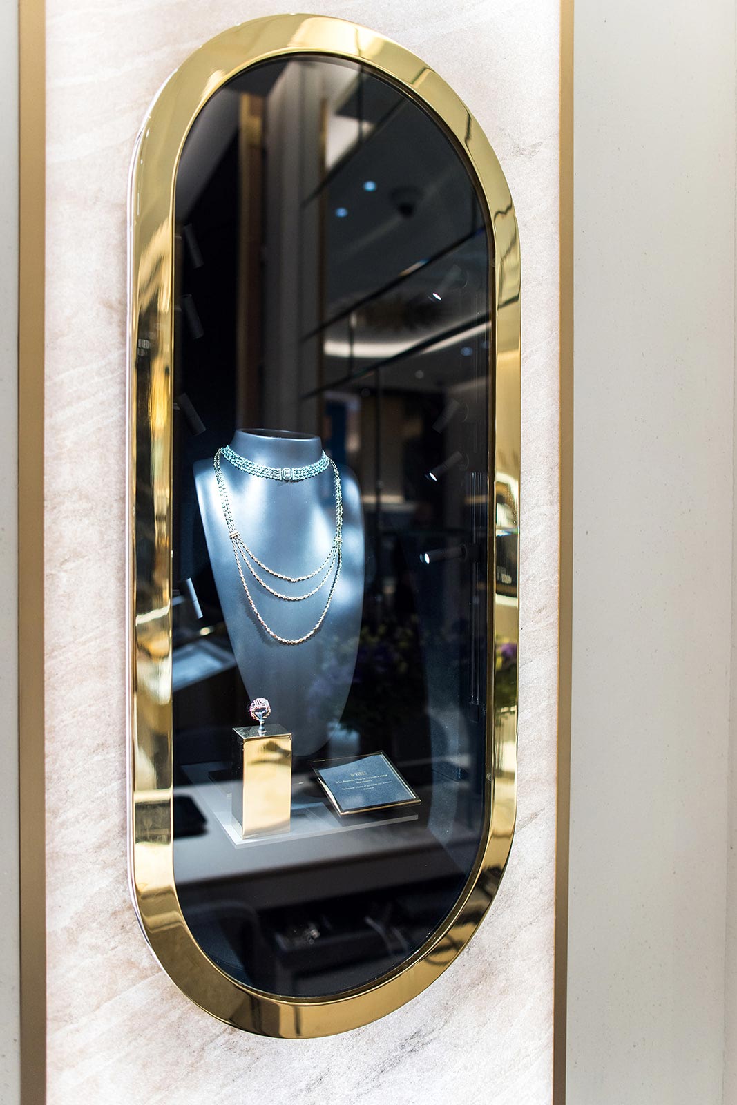Un focus sur une vitrine ovale verticale présentant un collier de diamants multi-rangs exposé sur un buste noir.