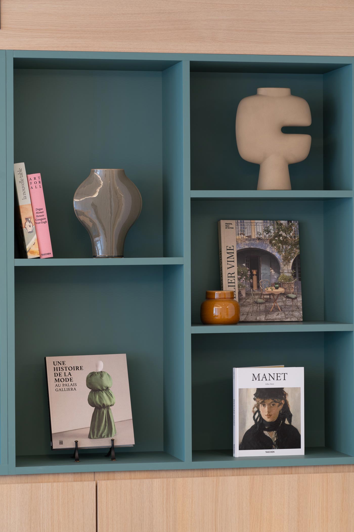 Une autre partie de l'étagère verte présentant des ouvrages sur la mode et Manet, accompagnés de poteries aux formes géométriques.
