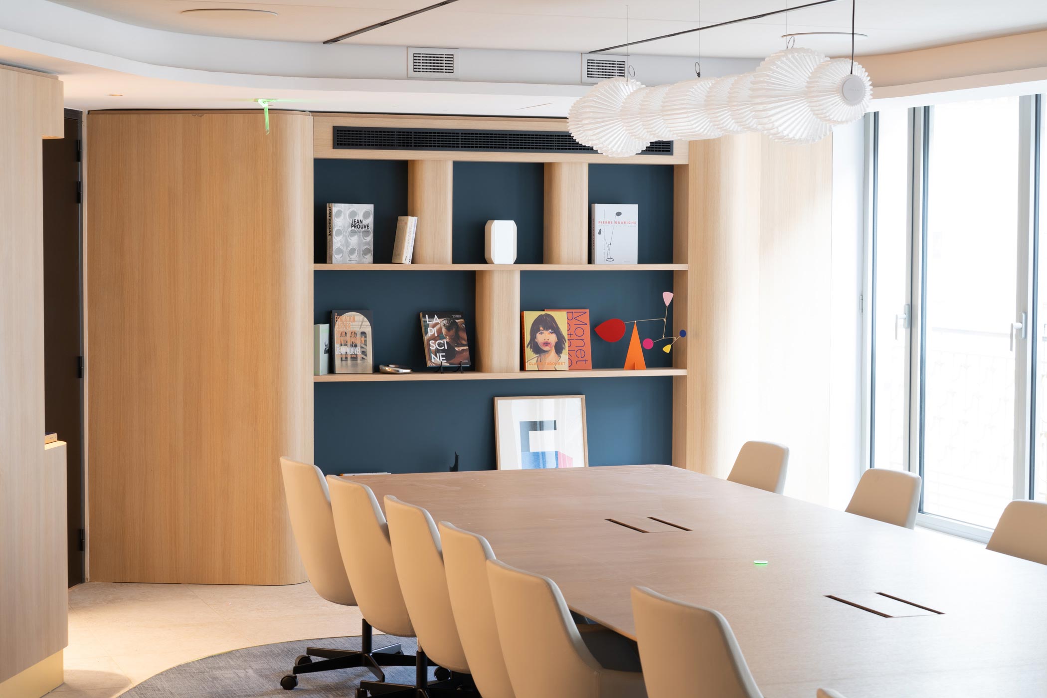 Une vue large d'une salle de conférence lumineuse avec une grande table en bois, des fauteuils ergonomiques beiges et une suspension design.
