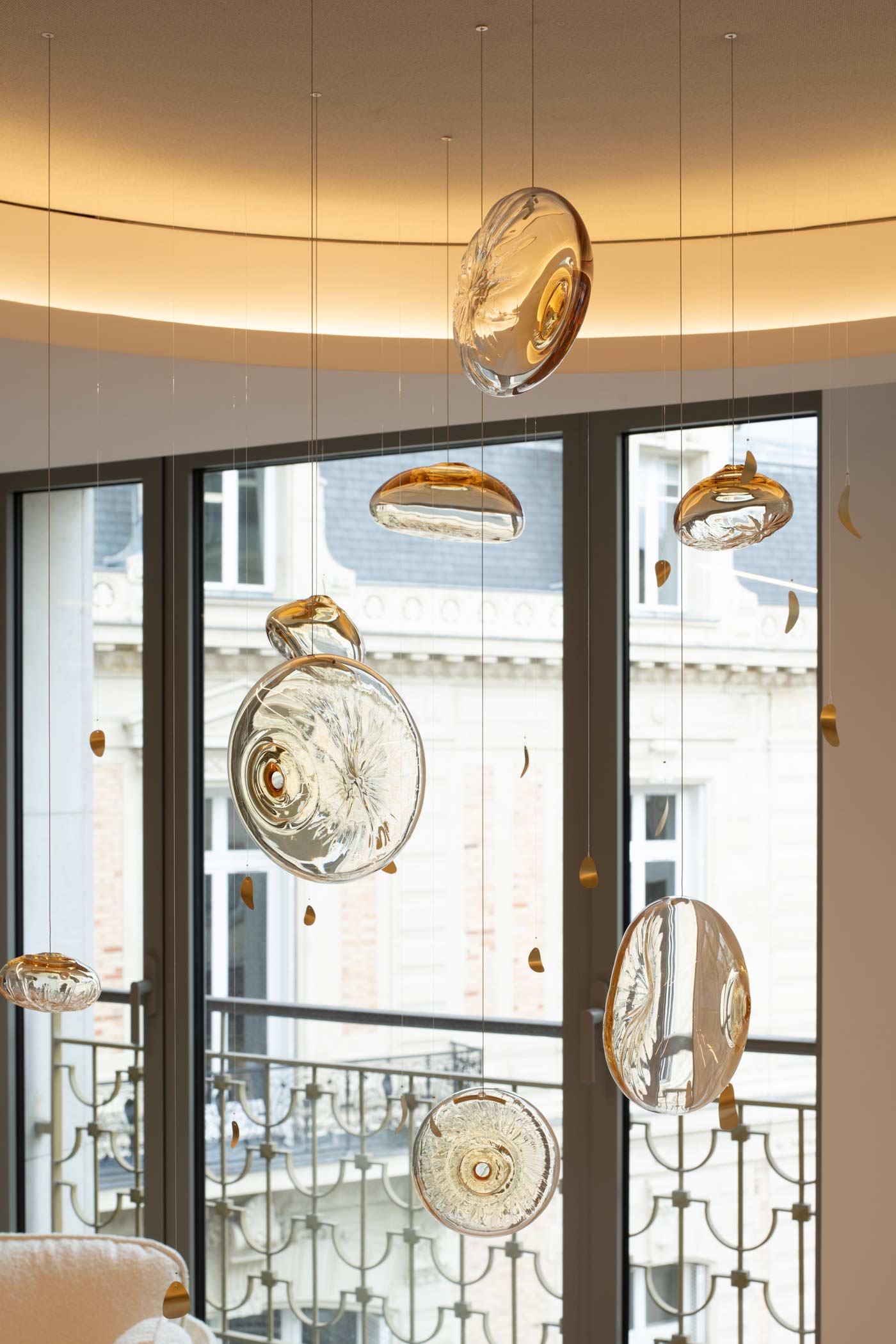 Un focus vertical sur les éléments en verre soufflé et les pépites dorées du luminaire, avec les façades parisiennes en arrière-plan.