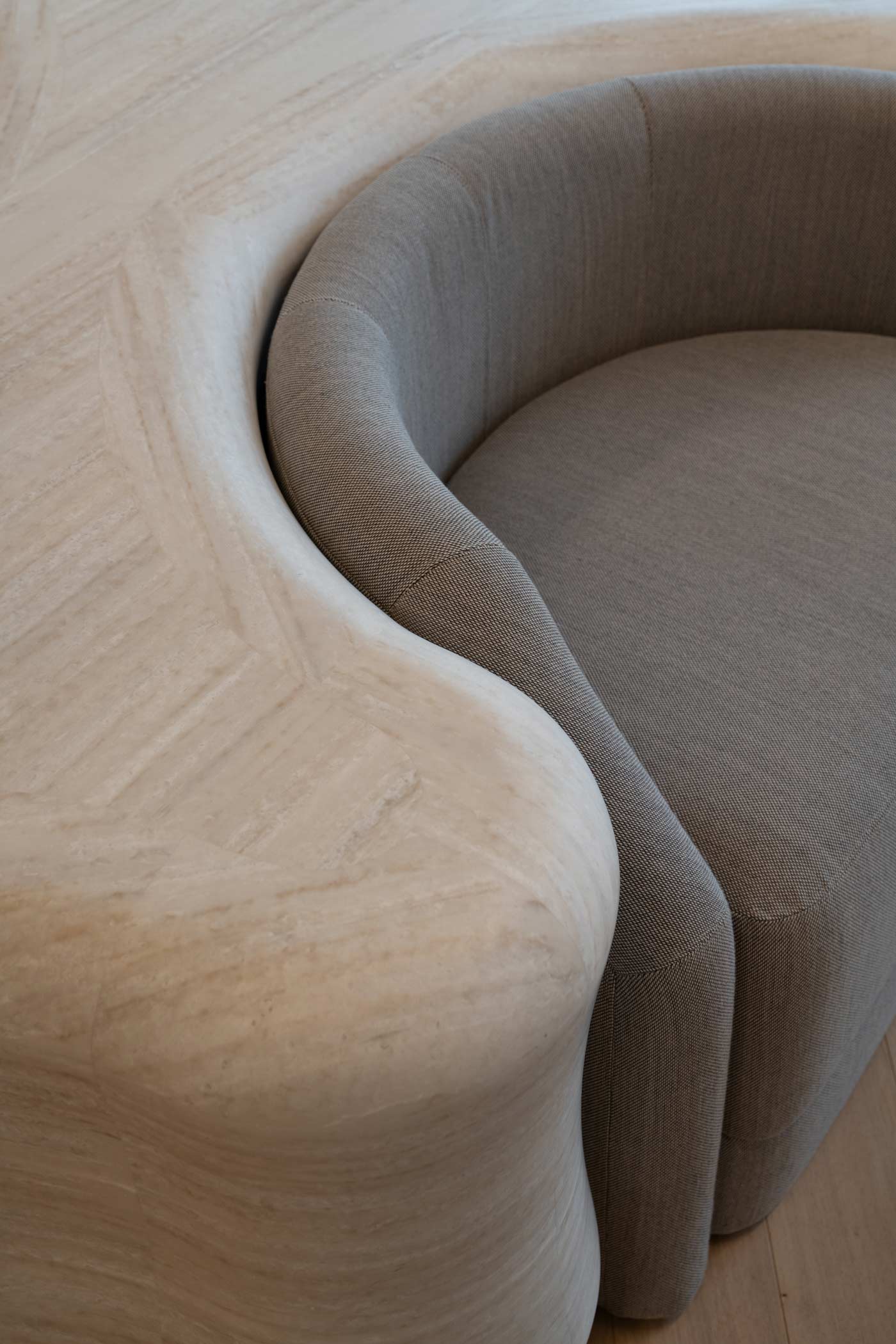 Un détail artistique montrant la rencontre entre les courbes douces d'une table en pierre naturelle et le textile gris d'un siège.